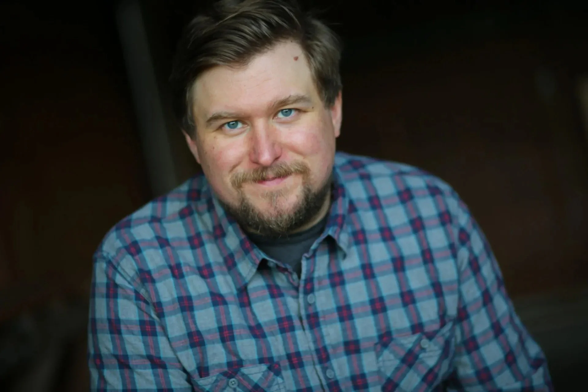 Michael Chernus with a beard standing against a dark background.