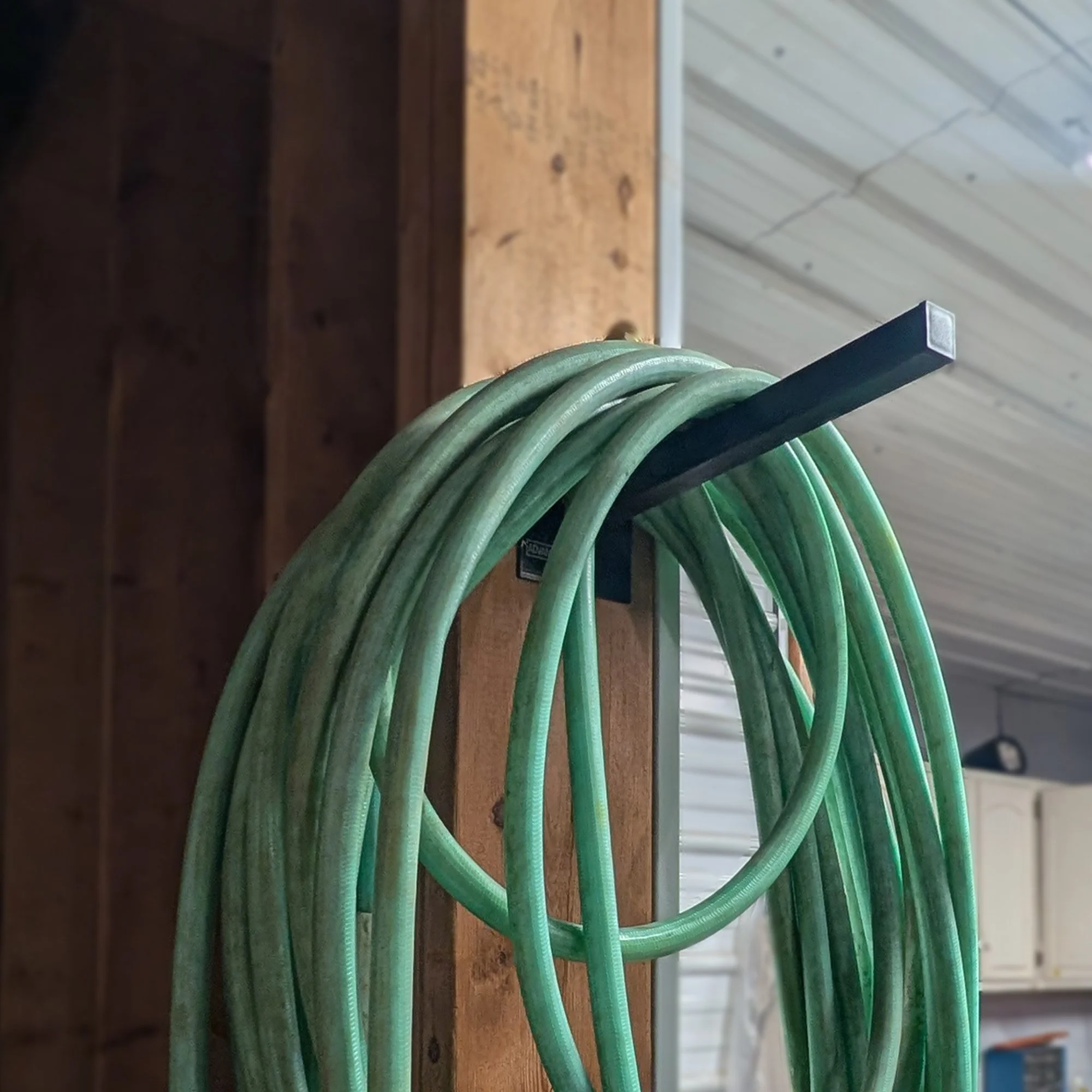 12-inch Single Prong Wall Mount Tool Rack in use holding a coiled green garden hose in a Michigan workshop, powder-coated black steel construction, made in Grand Rapids Michigan