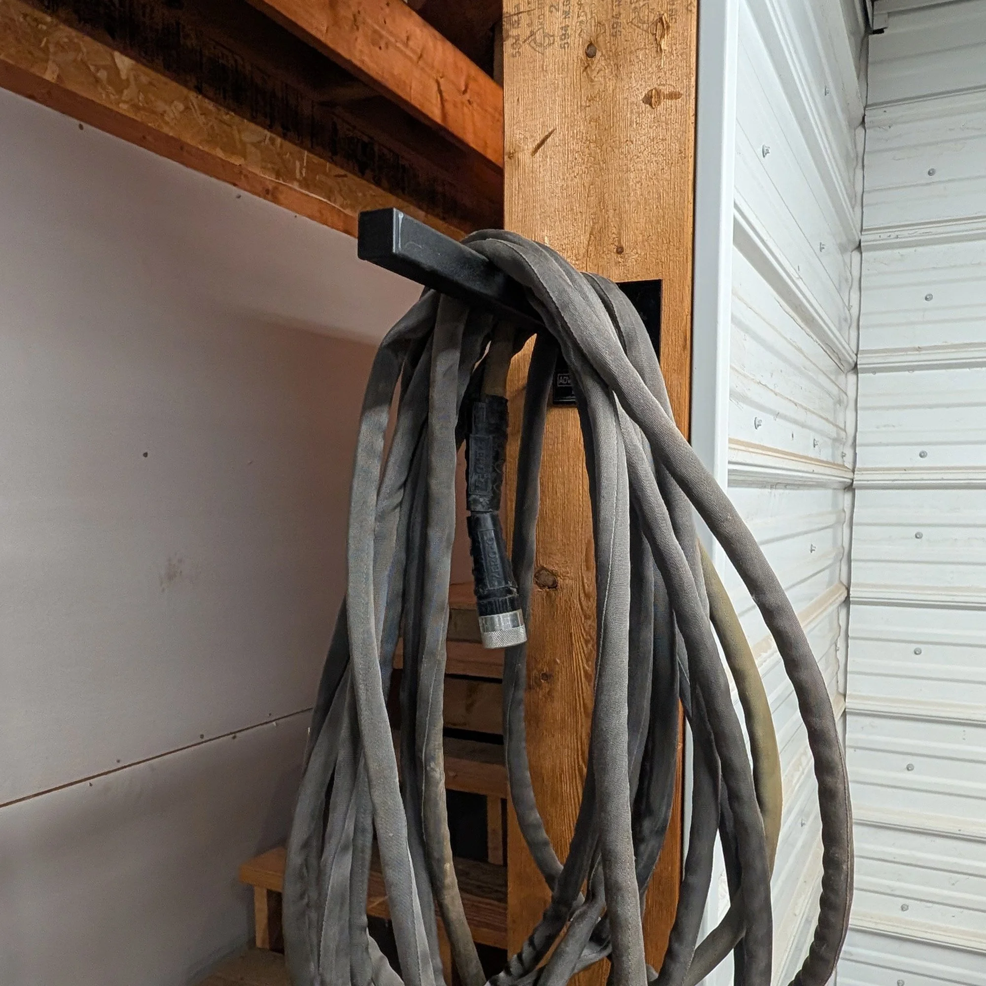 12-inch Single Prong Wall Mount Tool Rack in use holding a coiled black water hose in a workshop, demonstrating cord and hose storage capacity, made in Grand Rapids Michigan