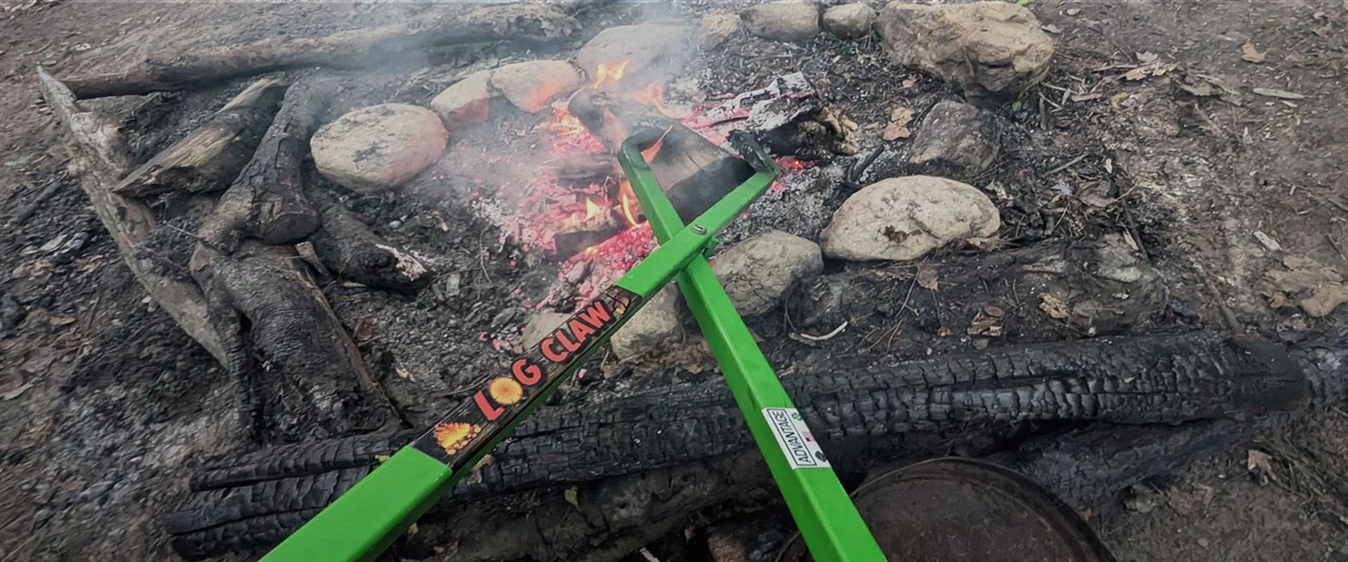 Lime green Advantage Log Claw grabbing a burning log from an outdoor fire pit — welded in Grand Rapids, Michigan