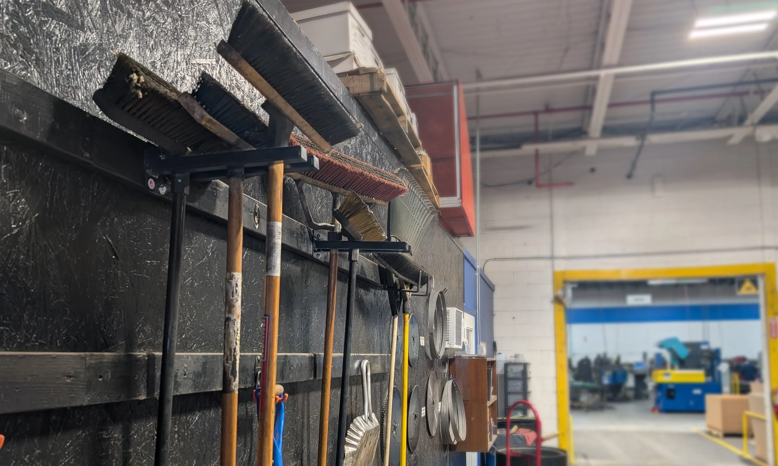 Wall-mounted tool rack organizing brooms and yard tools in workshop