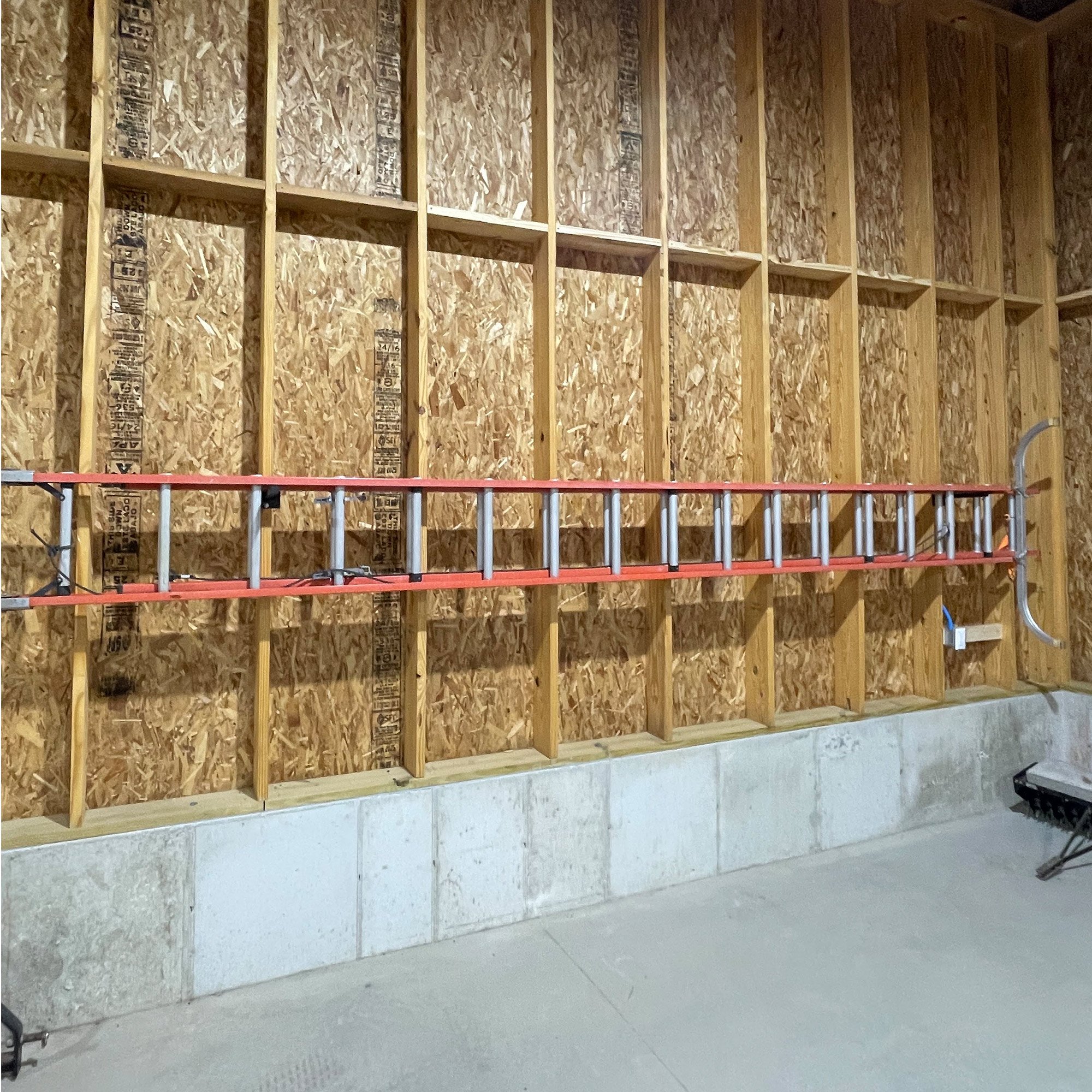 Two 12" Single Prong Tool Racks in black powder-coated steel mounted to a garage wall, holding a 36-foot extension ladder — customer install