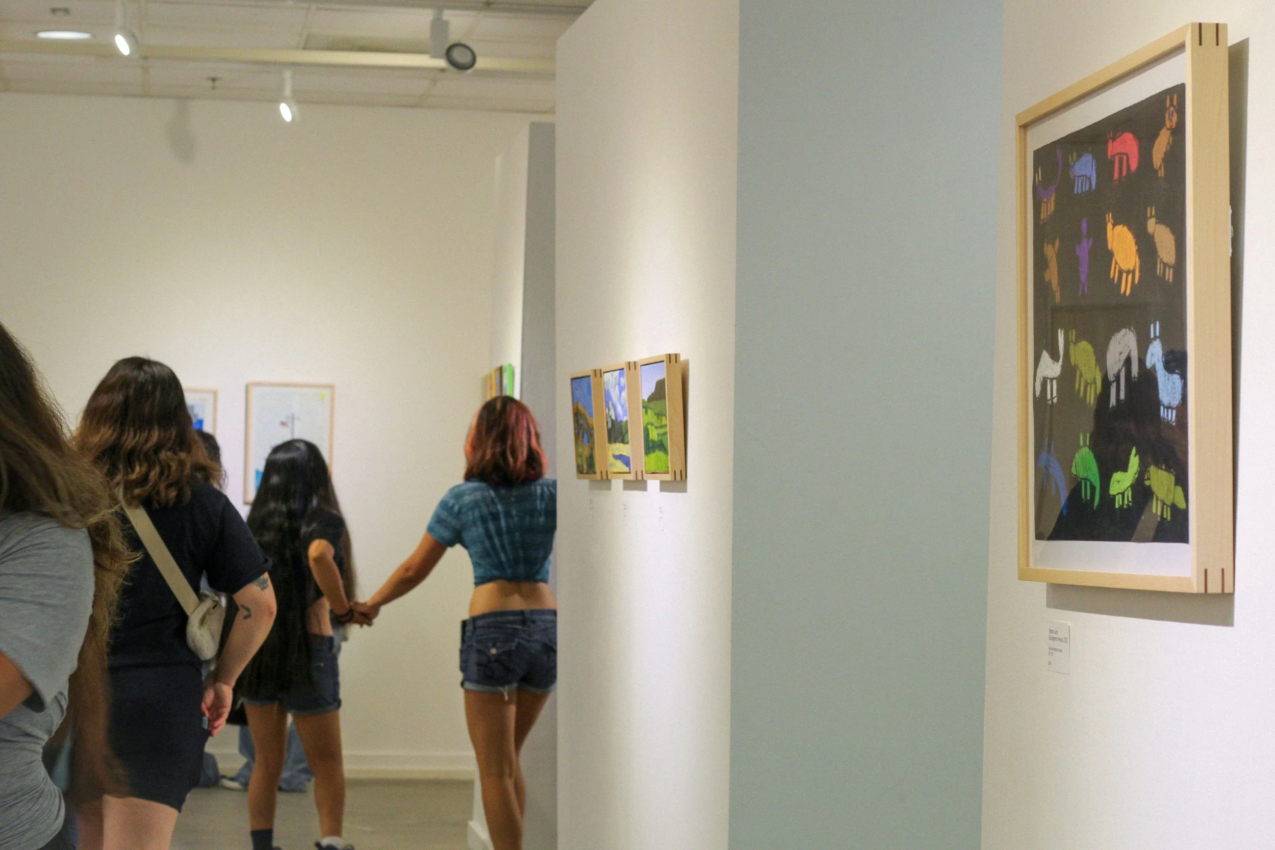 People viewing art exhibits in a gallery, with colorful paintings on the walls.