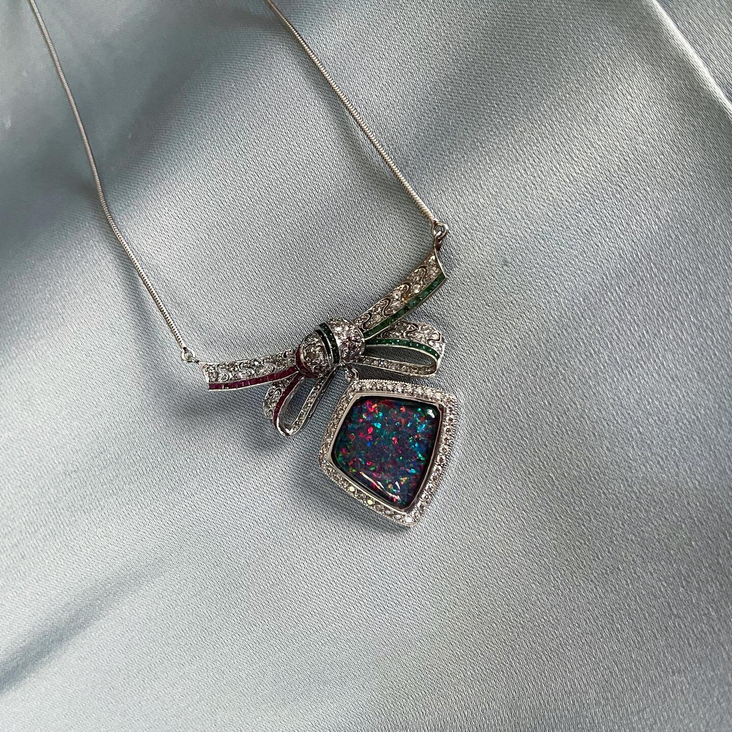 This necklace captures the beauty of an art deco diamond, sapphire, ruby, and emerald pin and bow. They now frame an extraordinary confetti opal, also entrusted in gold and diamonds to make an exquisite pendant. It is elegant, it is charming, it is h