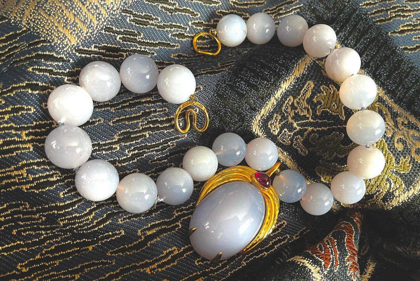 Chalcedony necklace with supersized dramatic beads accented by a wonderful centerpiece that can be worn with a necklace or elsewhere as it is an enhancer. It is framed in 18k gold with a sparkling cabochon ruby. The necklace and pendant are by Clunn,