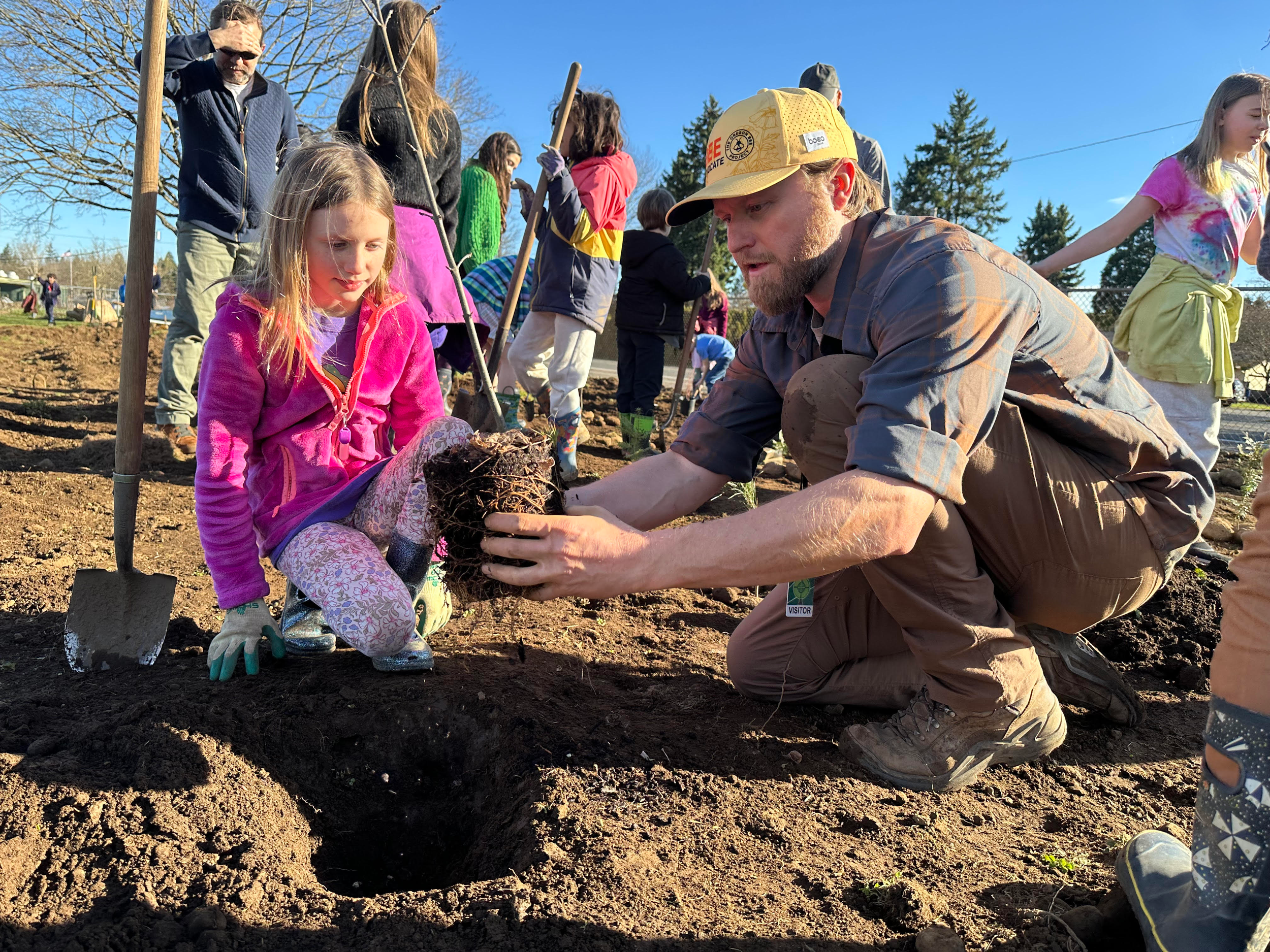 OICR Research Assistant Nic Tarter showing a student how to plant a sapling tree