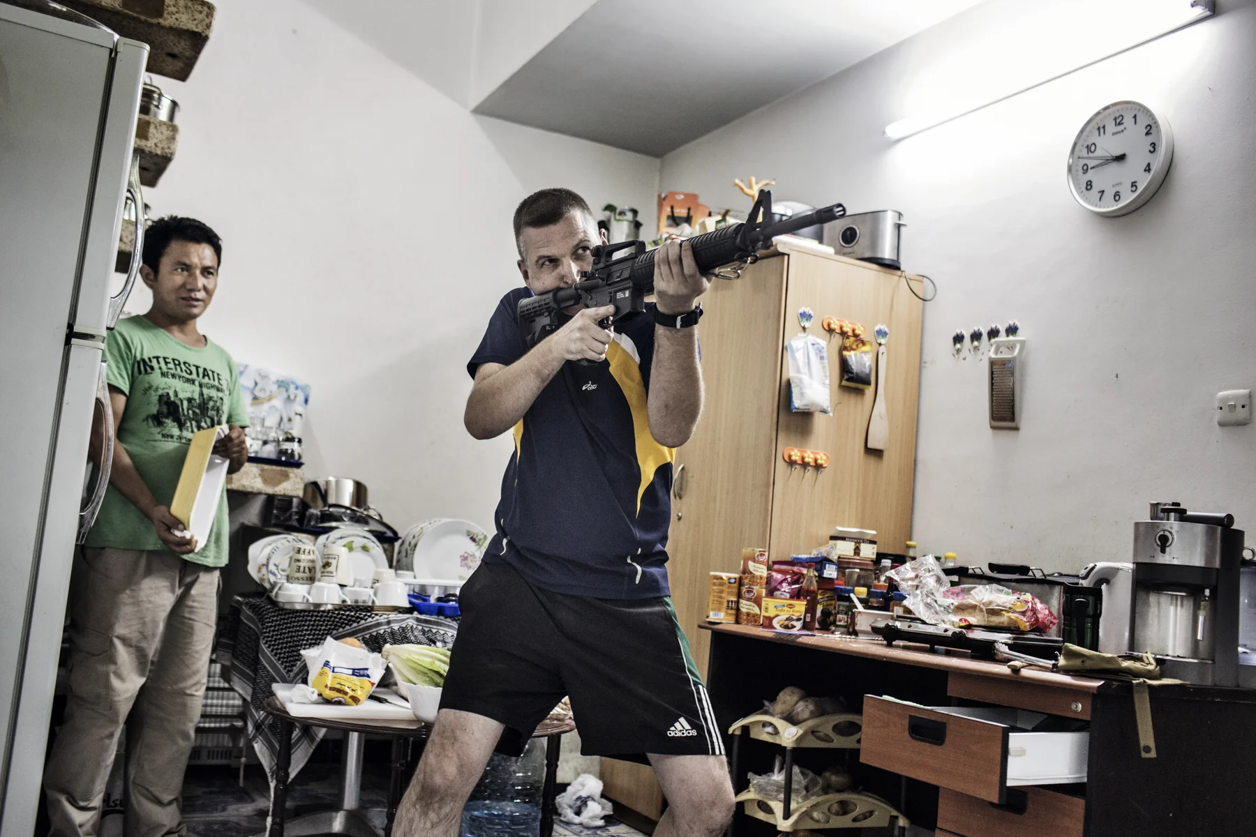 A member of a German-run private security company prepares his M-16 rifle, while a Nepali employee does the dishes. 