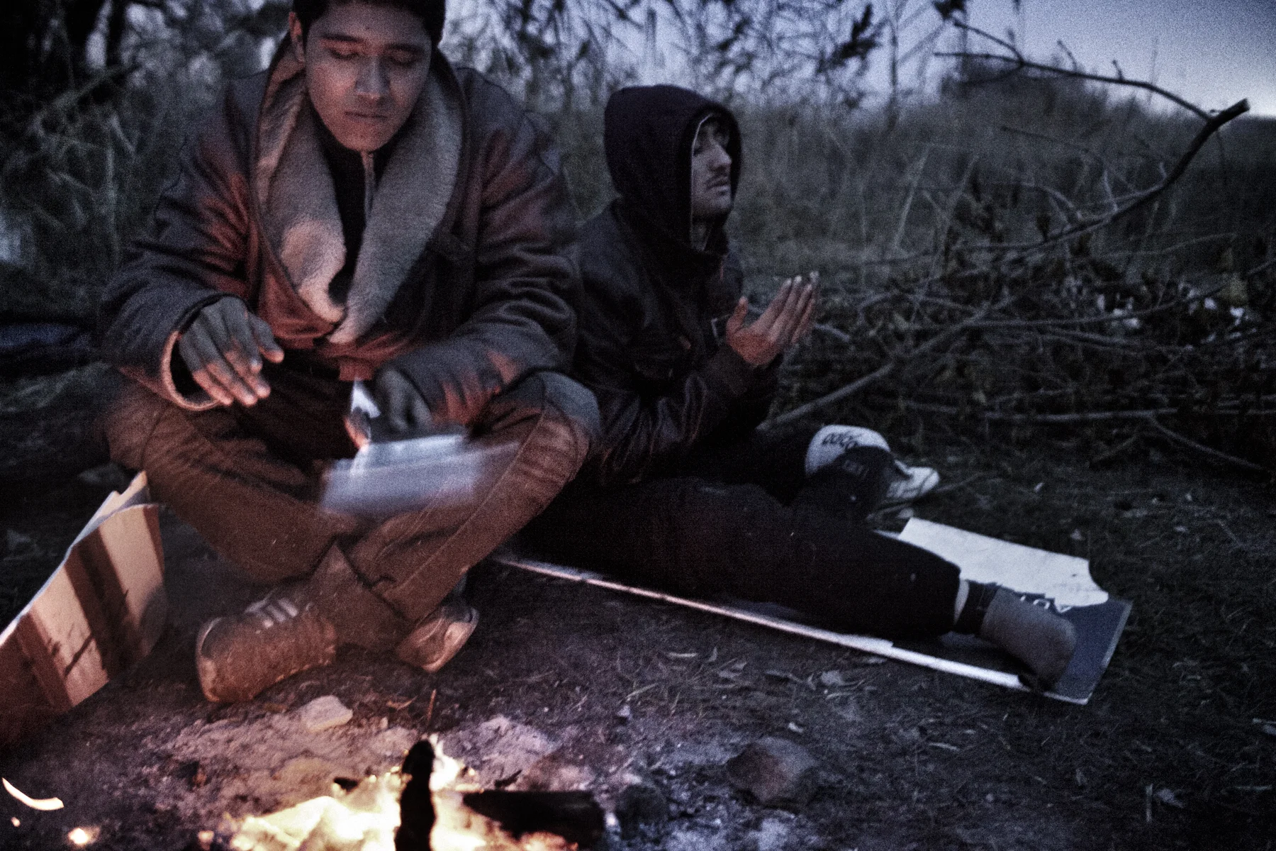 Kabir (left) and Zaher, Afghan refugees, sit at a fire, Subotica, Serbia.