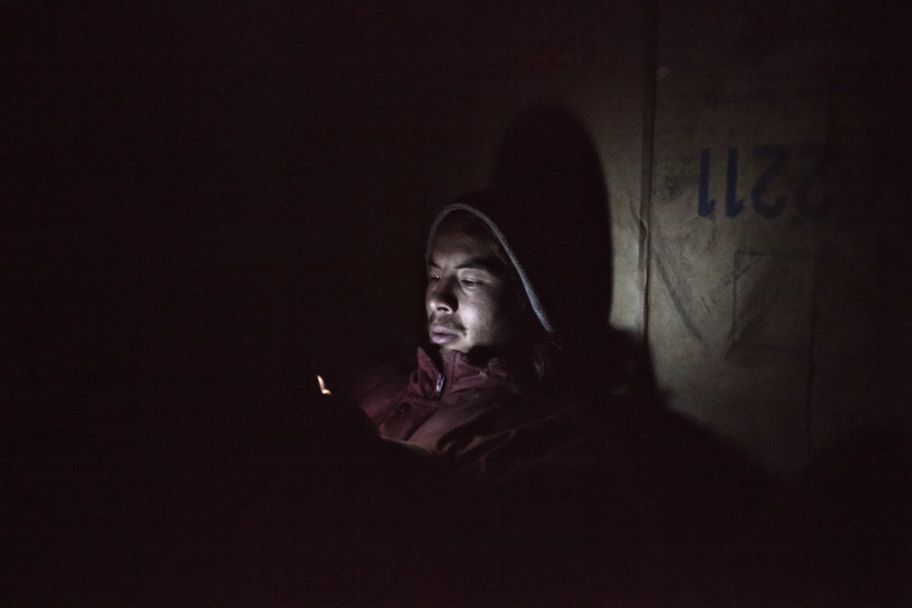 Jawad, an Afghan refugee, texts on his phone in a makeshift hut outside of Subotica, Serbia. Jawad came to Europe in 2005 and has been drifting between Greece, Serbia and Hungary unable to find asylum.