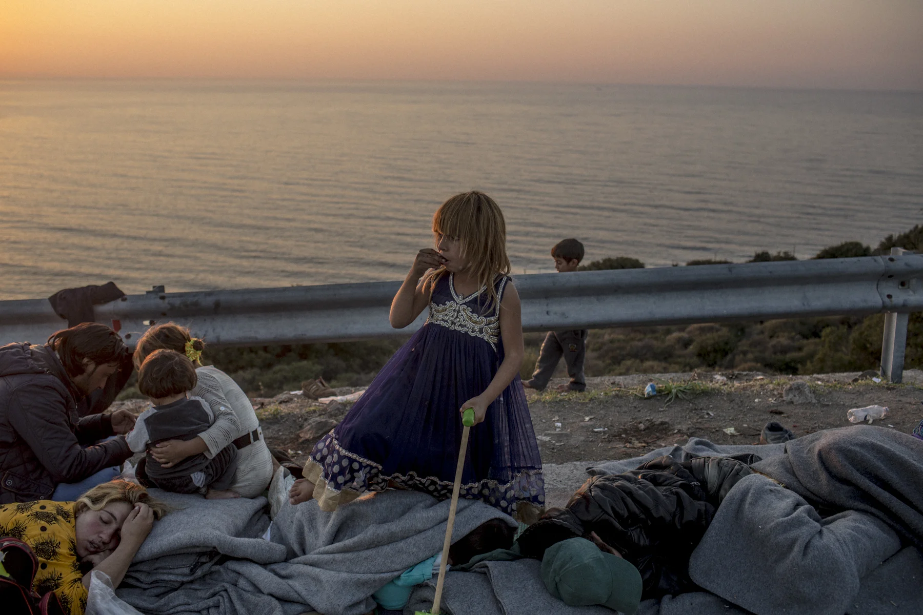 A young girl stands amongst her sleeping family on Lesbos. 