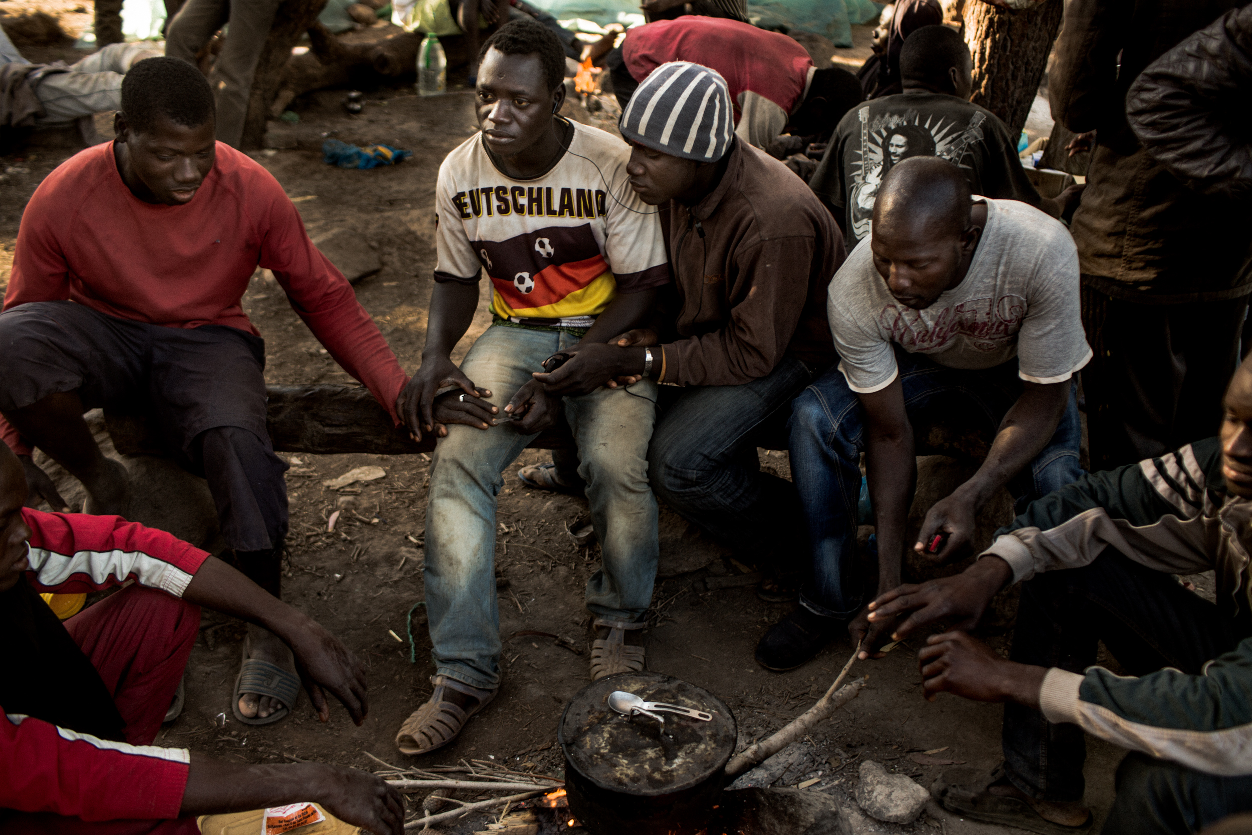 Malian men sit around a campfire in the unofficial migrant camp on the Gorougou Hill.