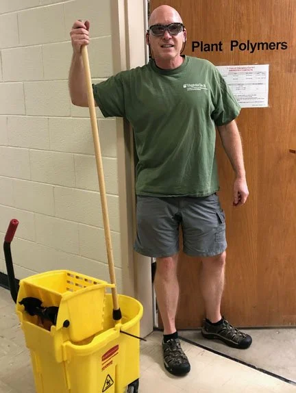 Frazier with mop & safety glasses at the lab door labeled Plant Polymers