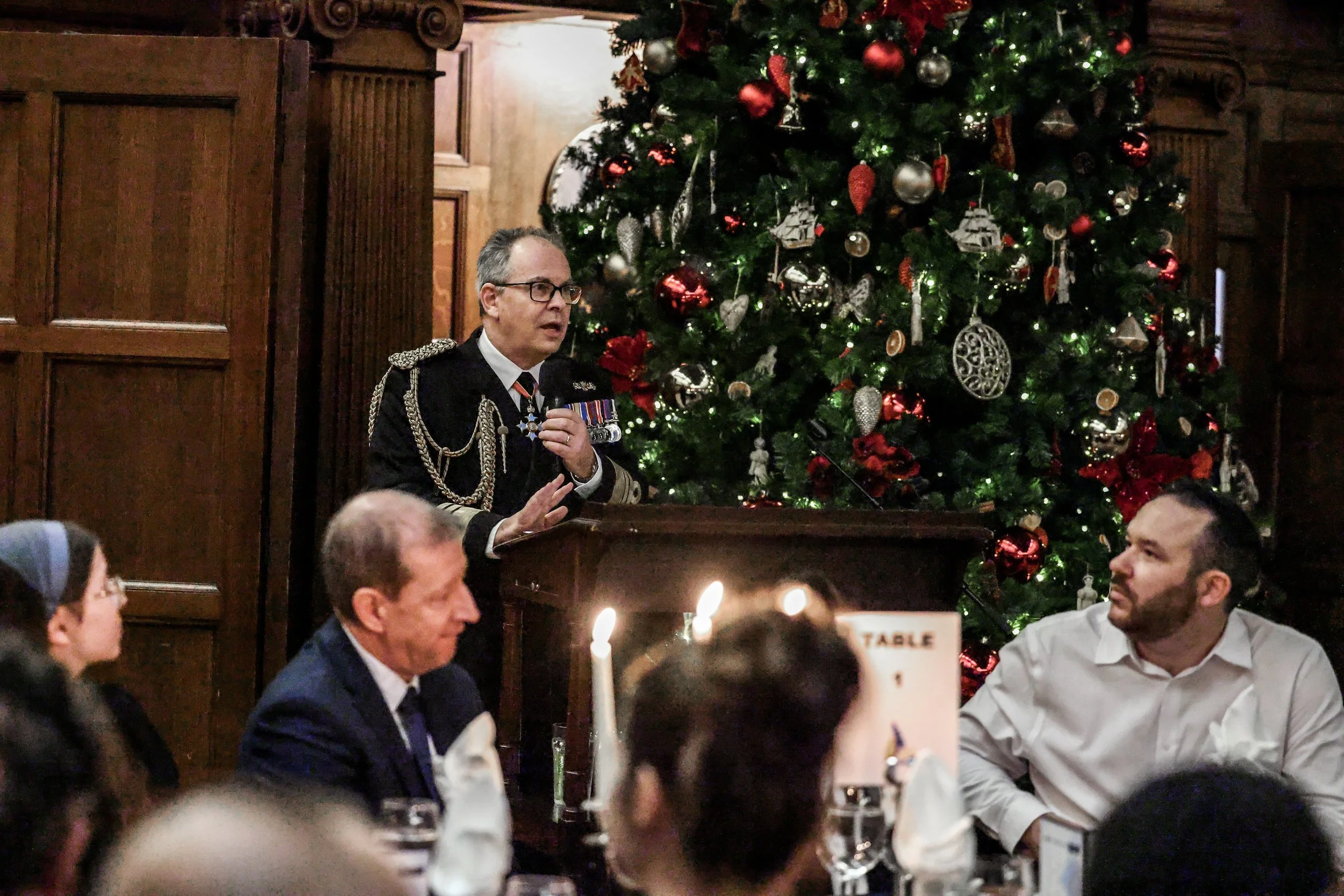 Second Sea Lord standing next to an ornate Christmas tree, delivering a speech to the attendees of the awards evening.