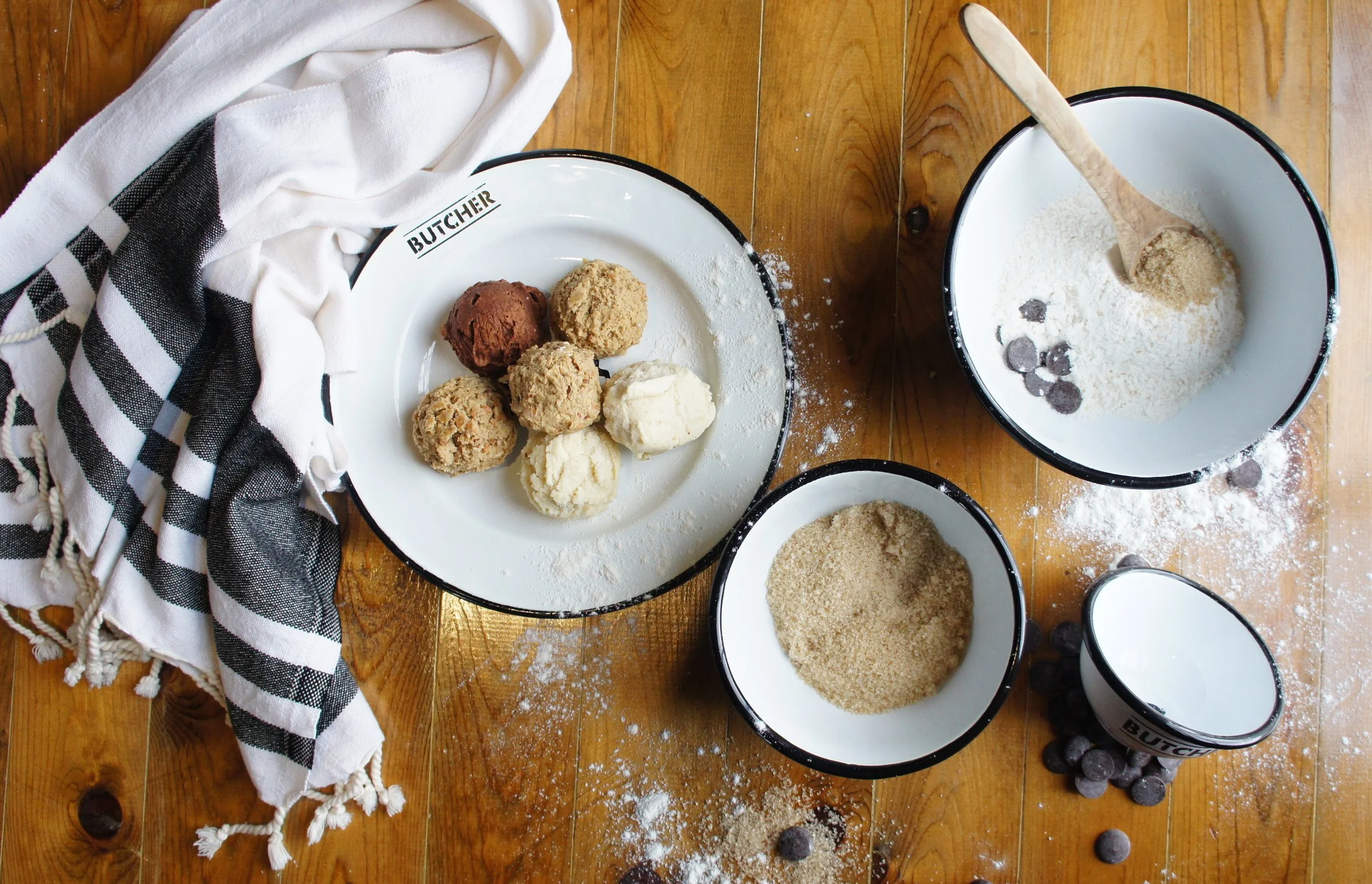 Overhead still life of custom Cochon Butcher enamelware bowls and plate with baking ingredients, chocolate chips, and a black-and-white Loomed NOLA towel, part of the shop’s 2015 retail product development.