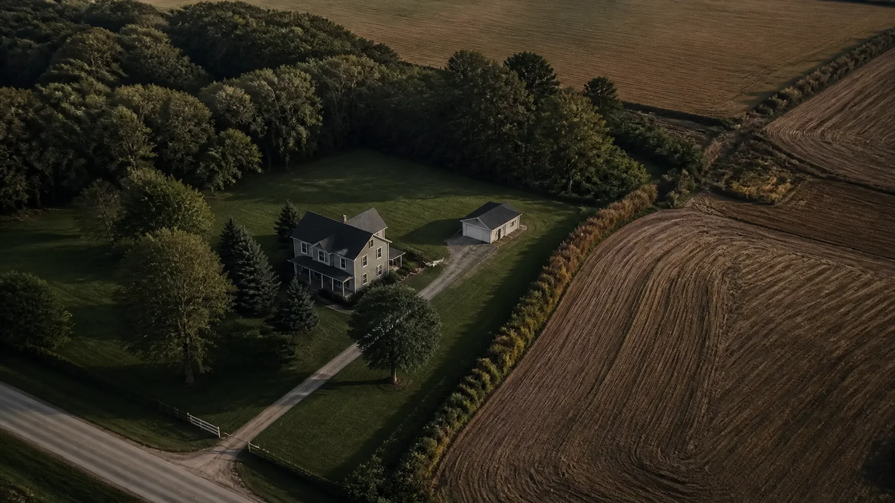 Aerial-oblique view of a Dufferin County rural property showing a farmhouse, immediate yard and driveway distinct from cultivated fields