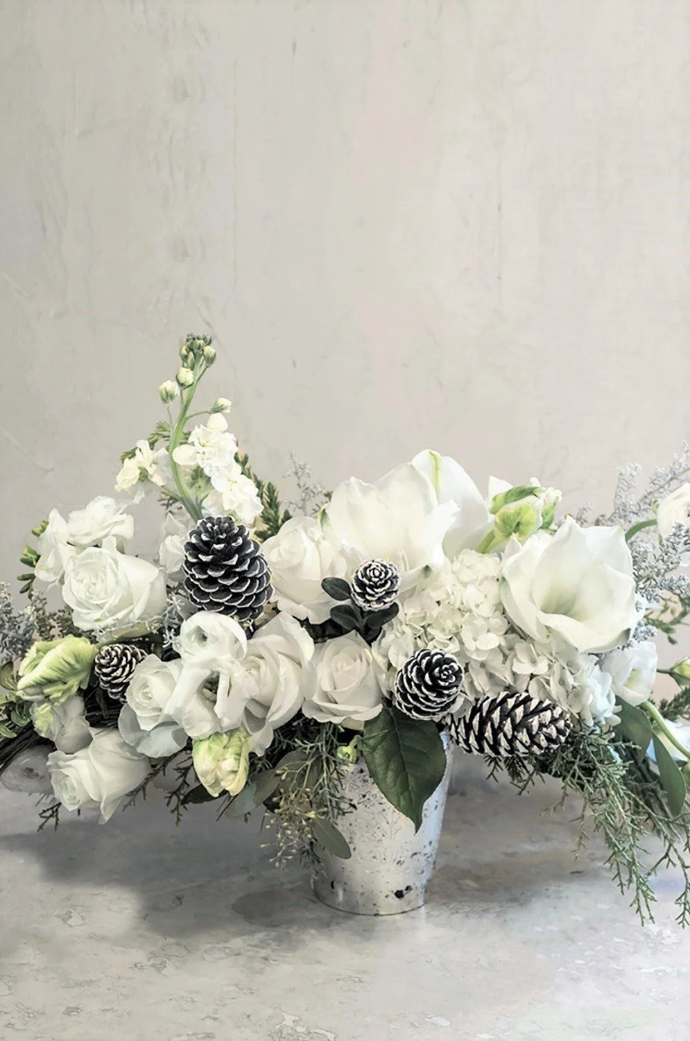 white amaryllis roses holiday flower arrangement flocked pinecones cedar