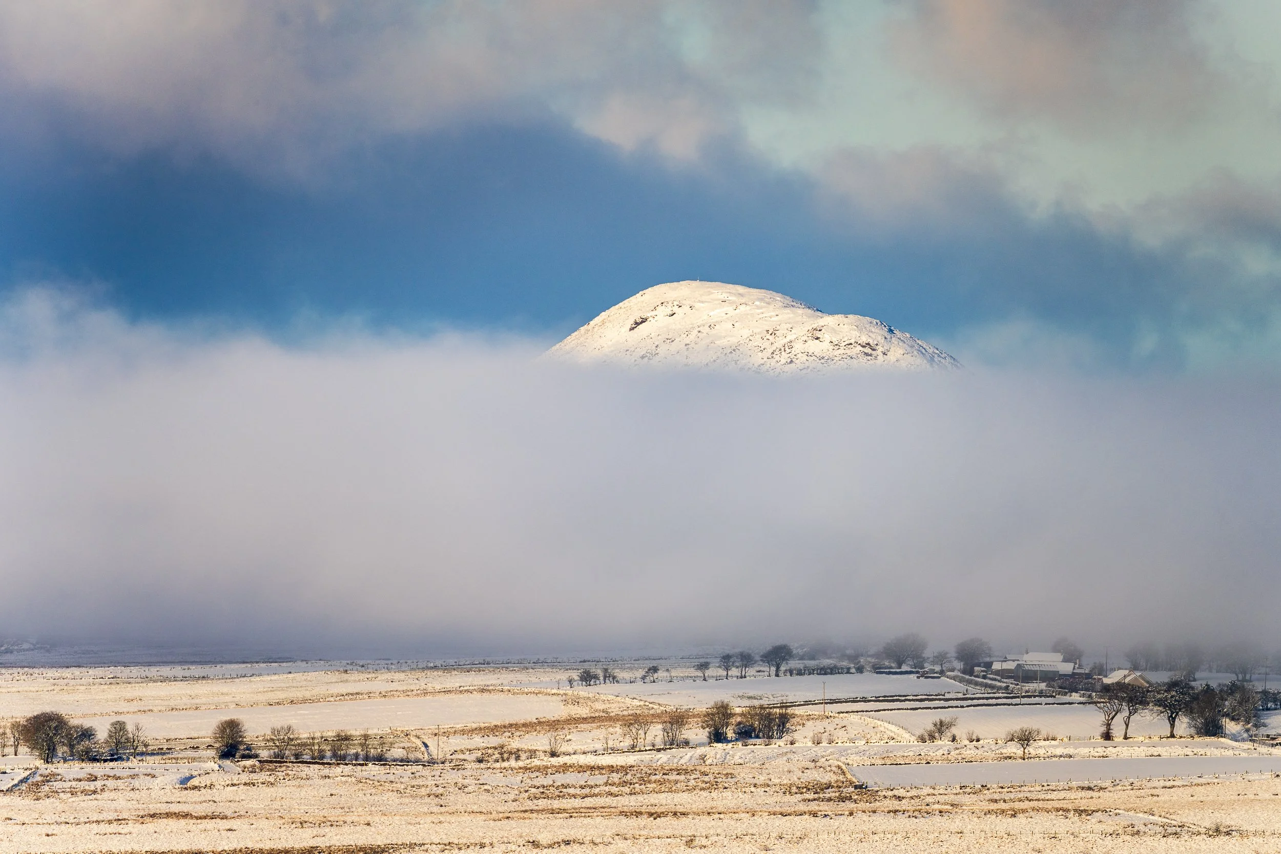 A snow capped Slemish peeks above the cloud