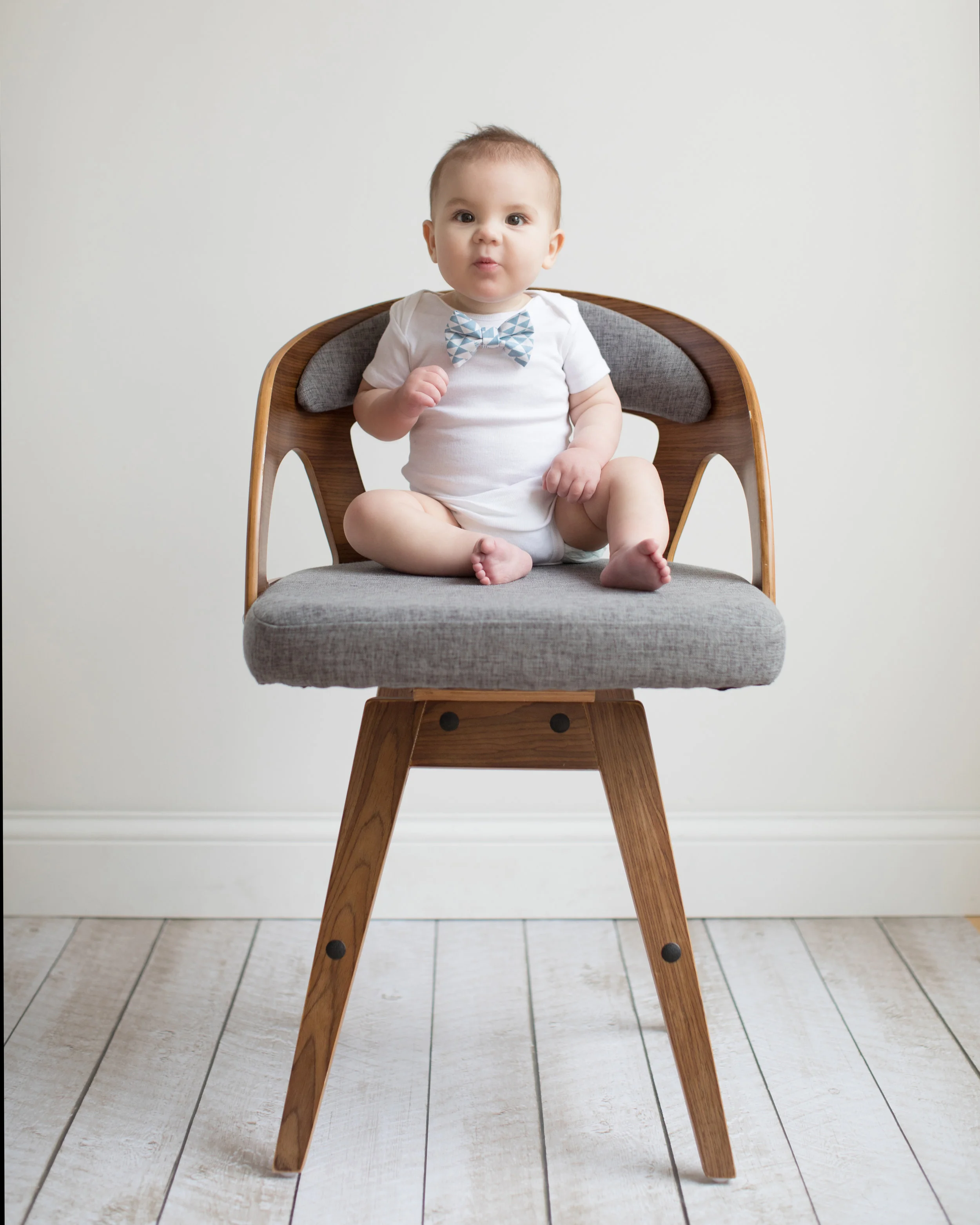 Baby boy in white onesie sitting on chair during natural light studio portrait session