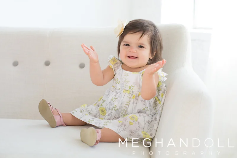one-year-old-girl-claps-on-white-couch