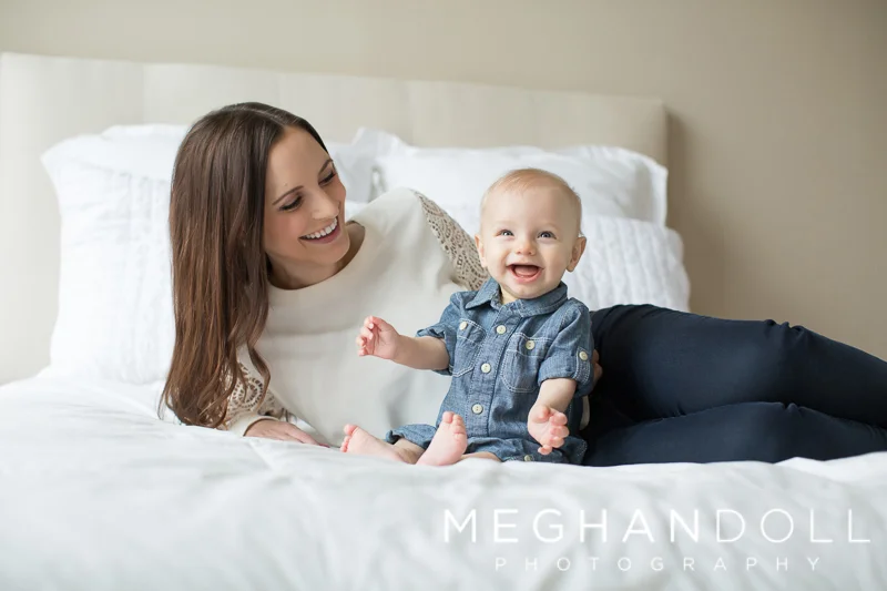 mom-laughs-with-six-month-old-son-on-white-bed