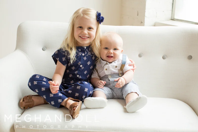 big-sister-cuddles-baby-brother-on-white-button-couch