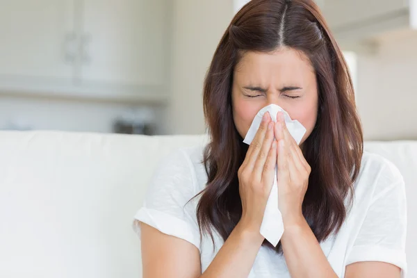 brunette woman sneezing into tissue to illustrate upper respiratory infection or allergies