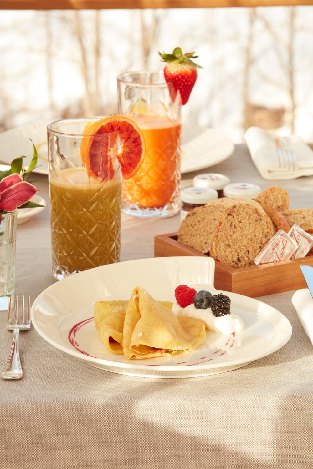 Breakfast with a plate of crepes served with cream and berries and orange juice in two glasses with orange slices on the rim