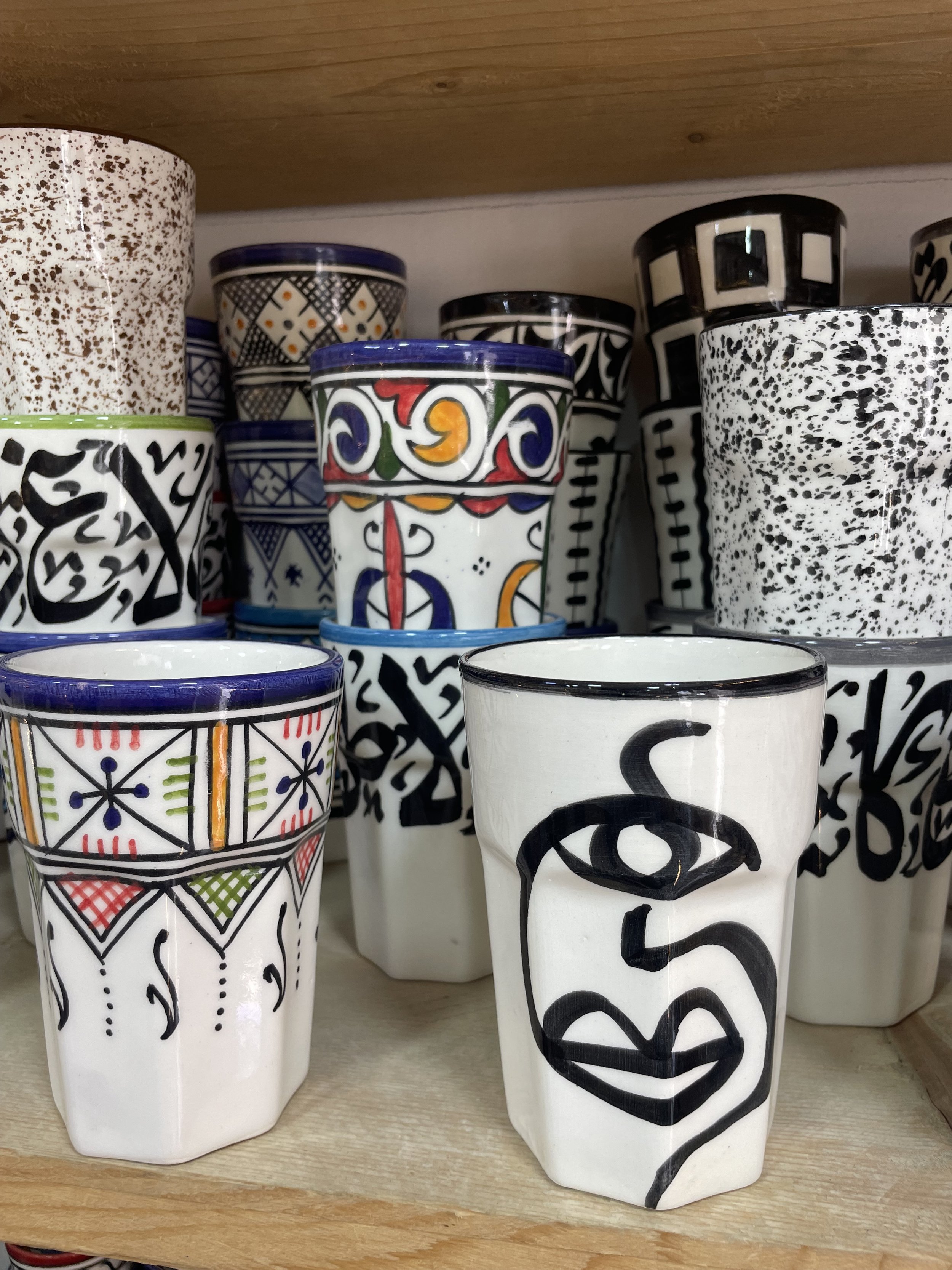 Small white coffee cups with colour details on them sitting on a shelf