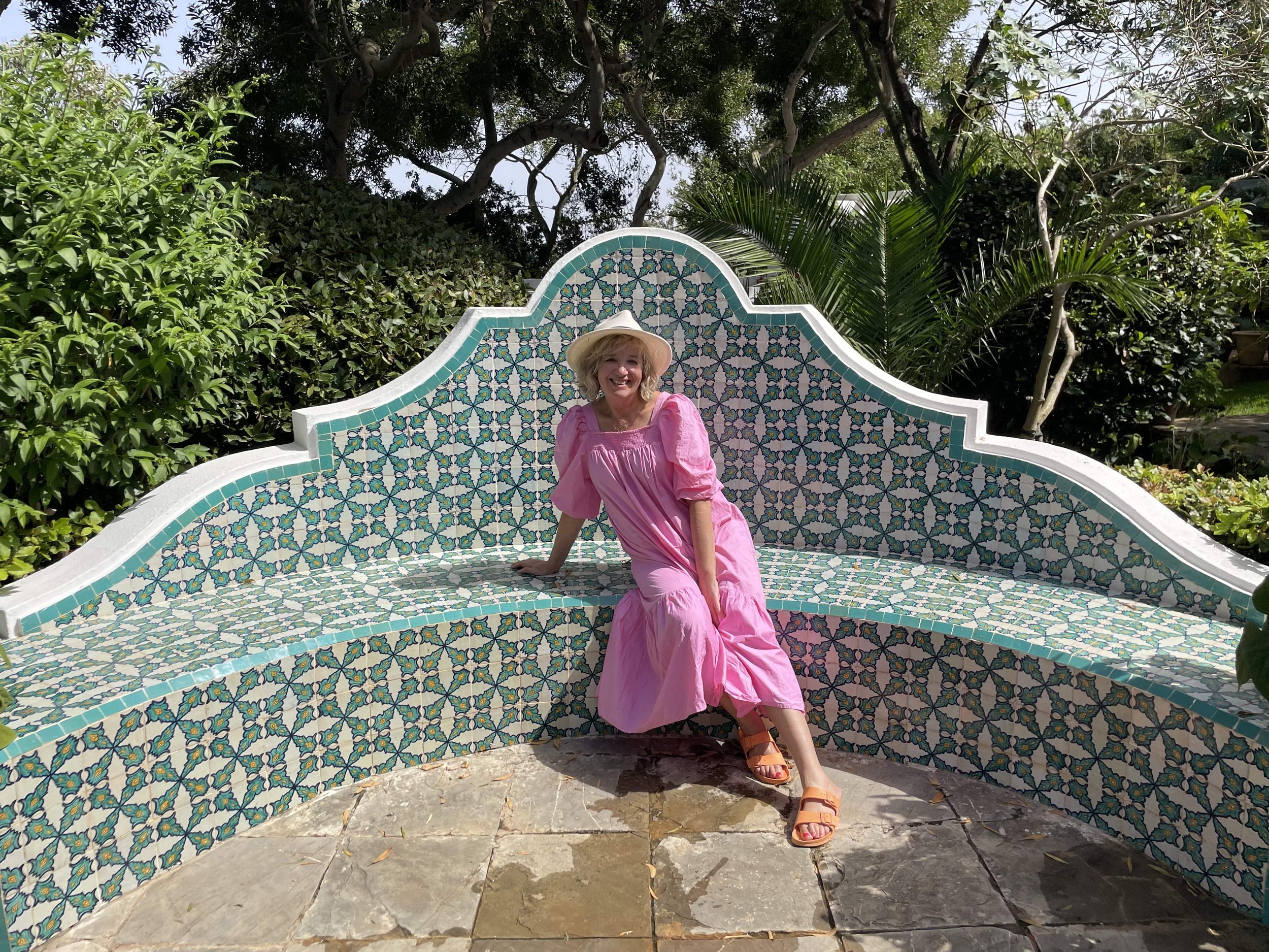 Wendy Rigg wearing a pink dress sitting on a light blue titled marble bench