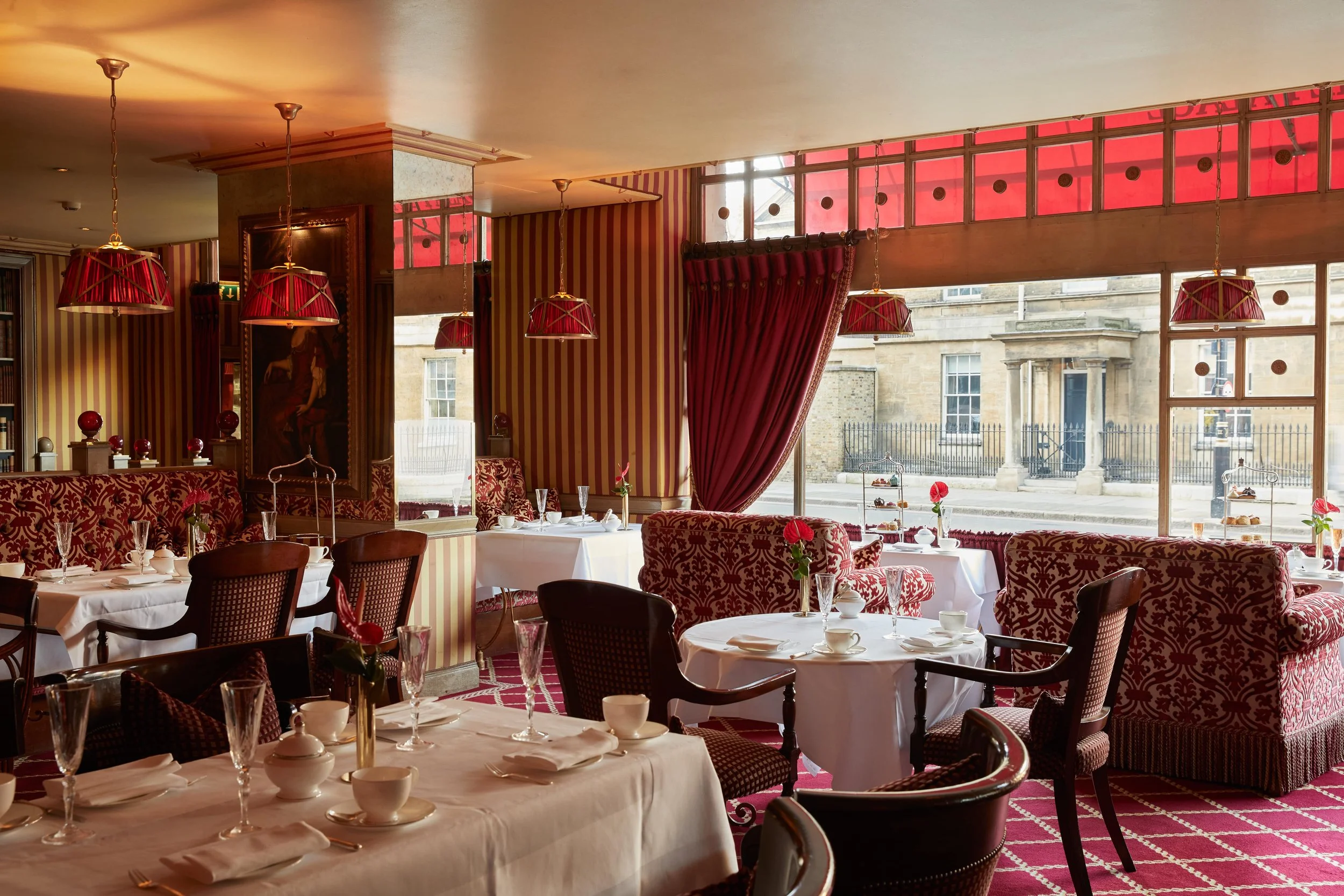A lounge with red and white decor and tables ready with teacups, champagne glasses and plates along with a red flower on each table