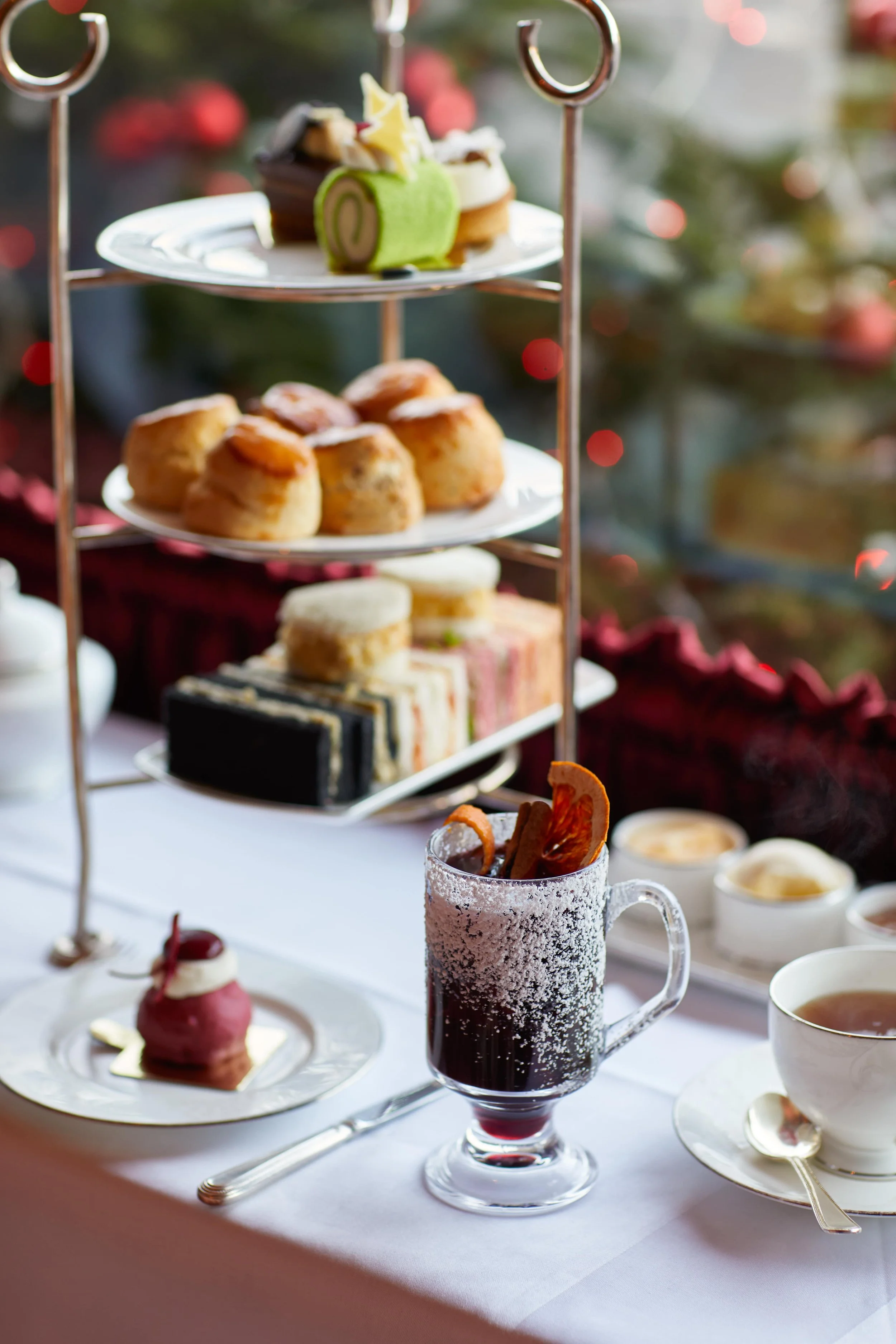 A glass of mulled wine coated with sugar pewter in front of a cake stand with cakes, scones and finger sandwiches