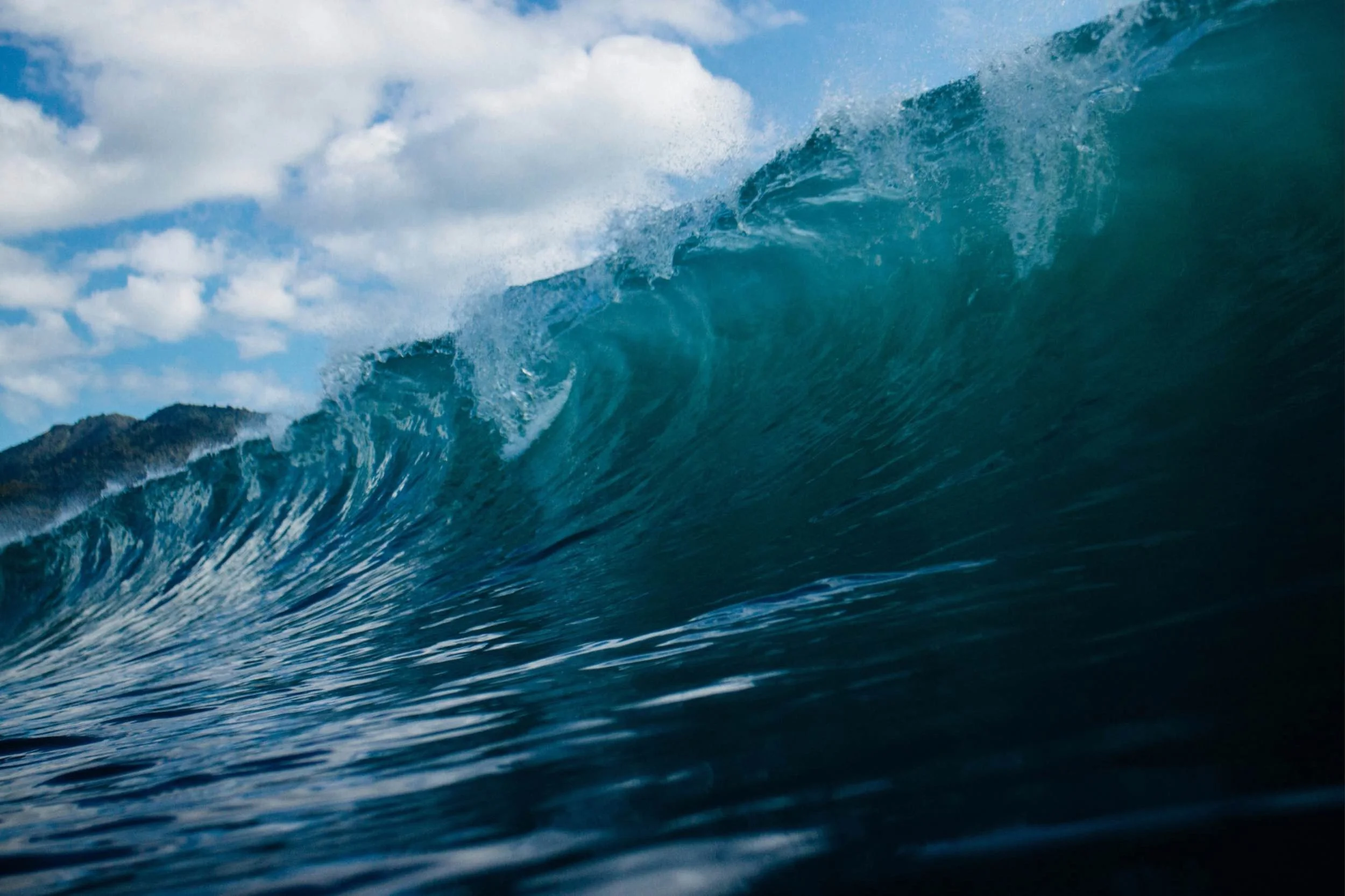 Close up of a swell of blue waves forming against a lightly cloudy blue sky