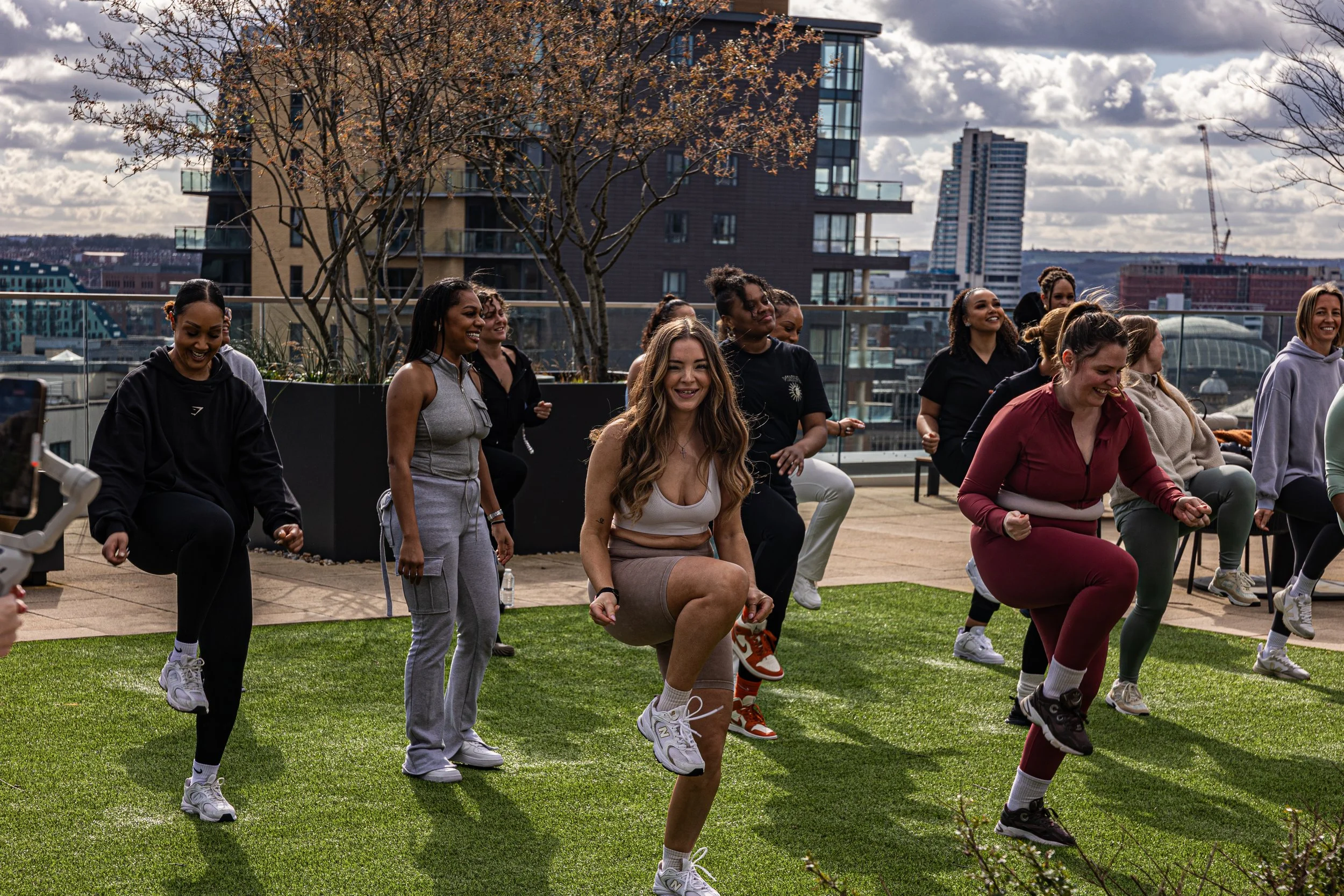 A group of women exercising outdoors on a rooftop in the city, doing leg lifts and smiling.