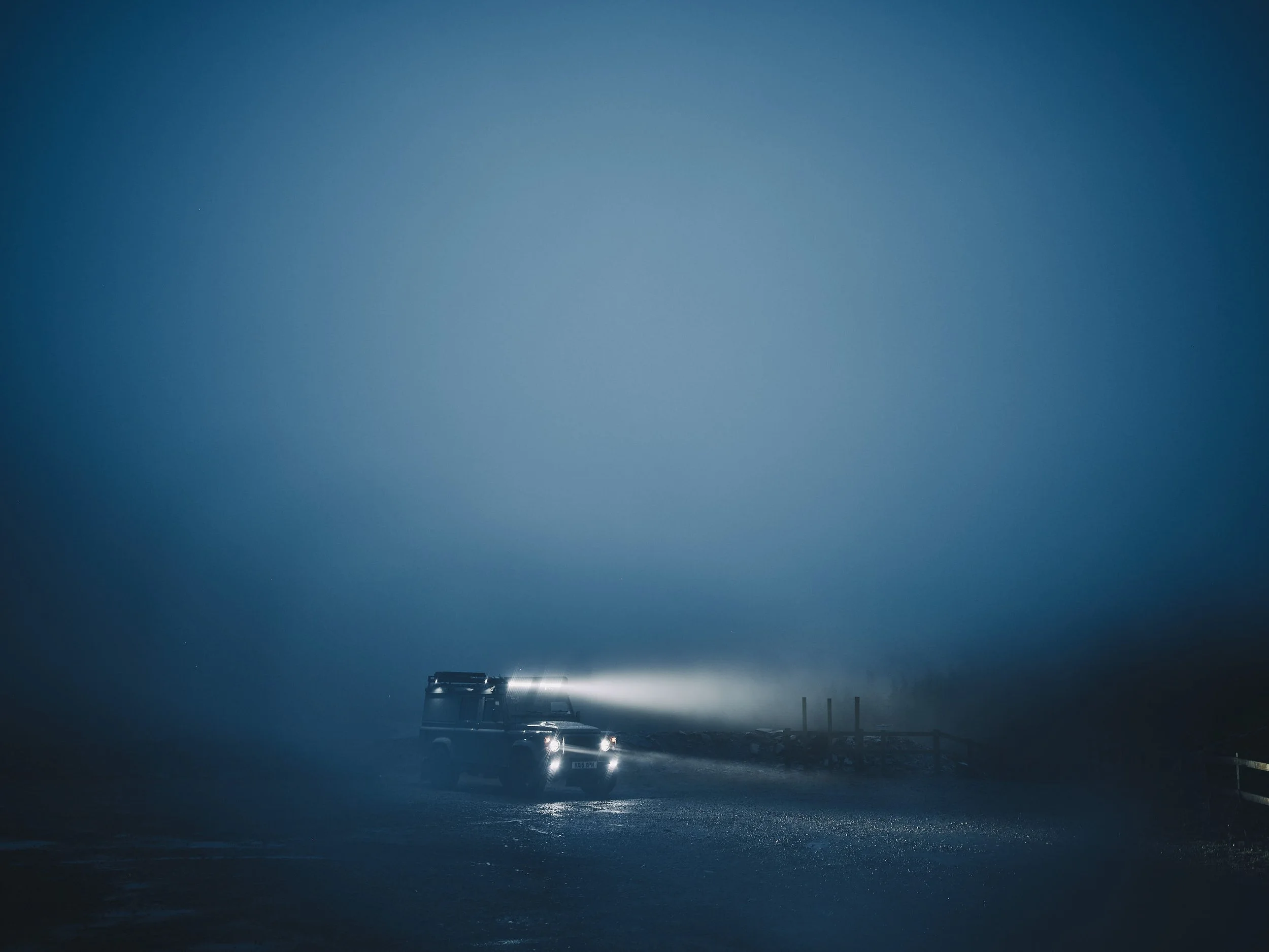 dramatic image of a Land Rover defender, with light bars lighting up the foggy twilight sky travel story by automotive photographer Matthew Lloyd