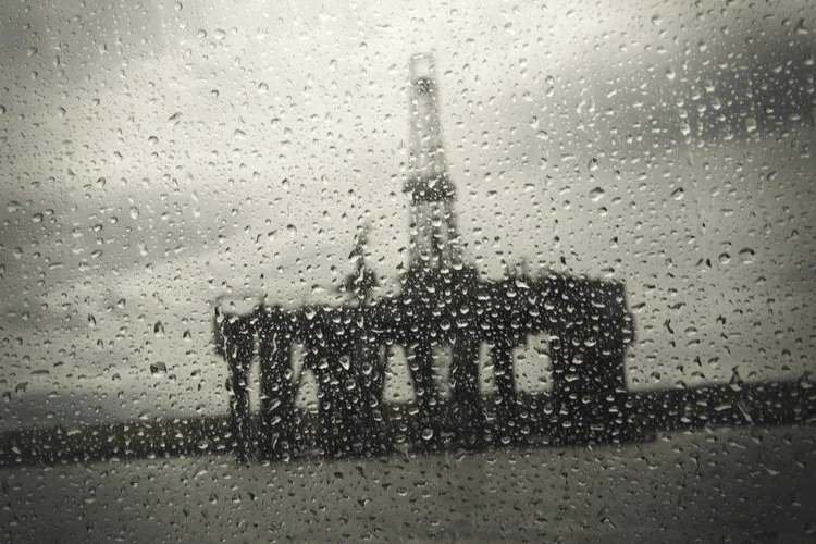 Offshore oil rig viewed through raindrop-covered window, creating a blurry effect.