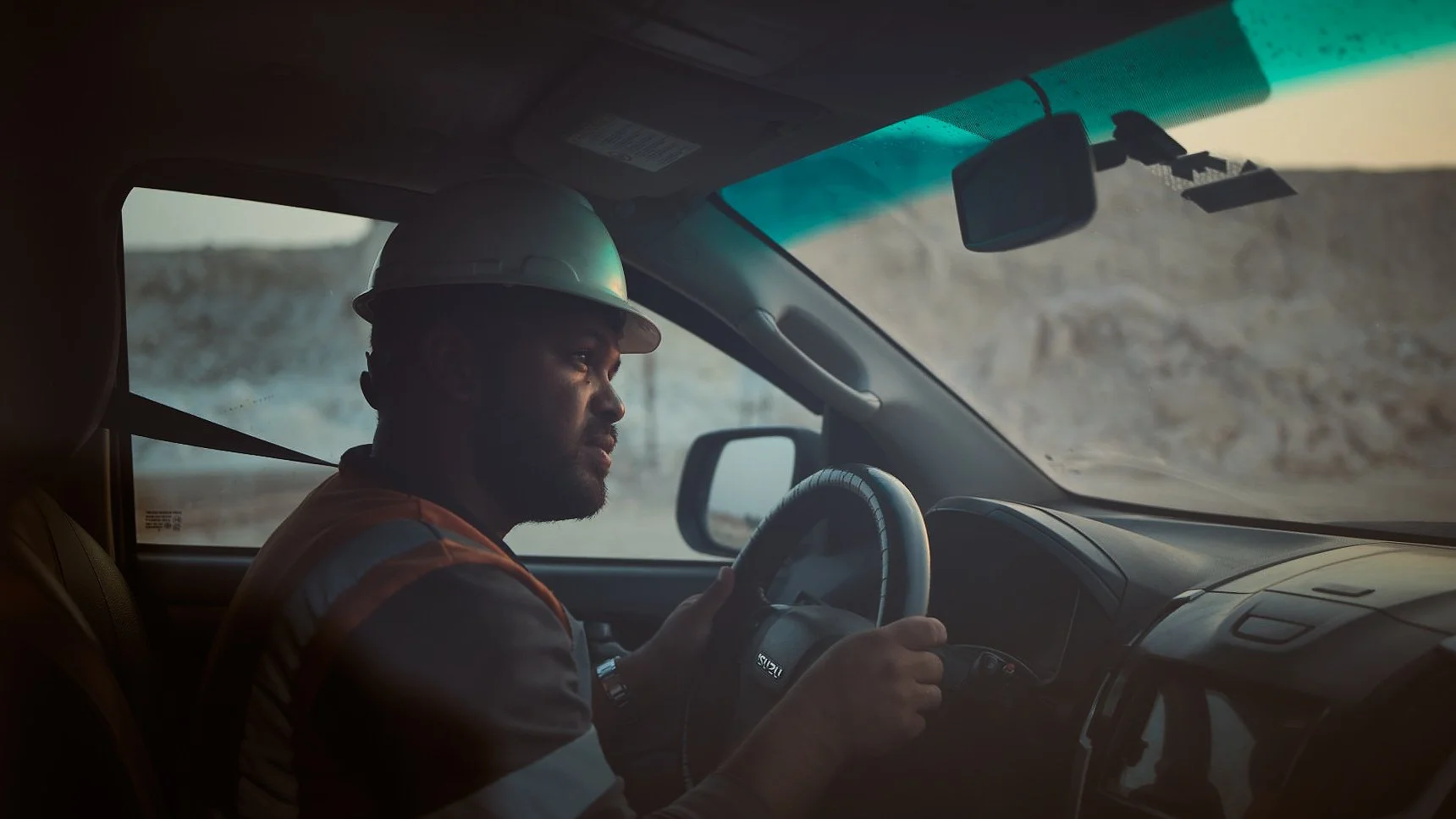 Man in hard hat driving a vehicle, focused on road.