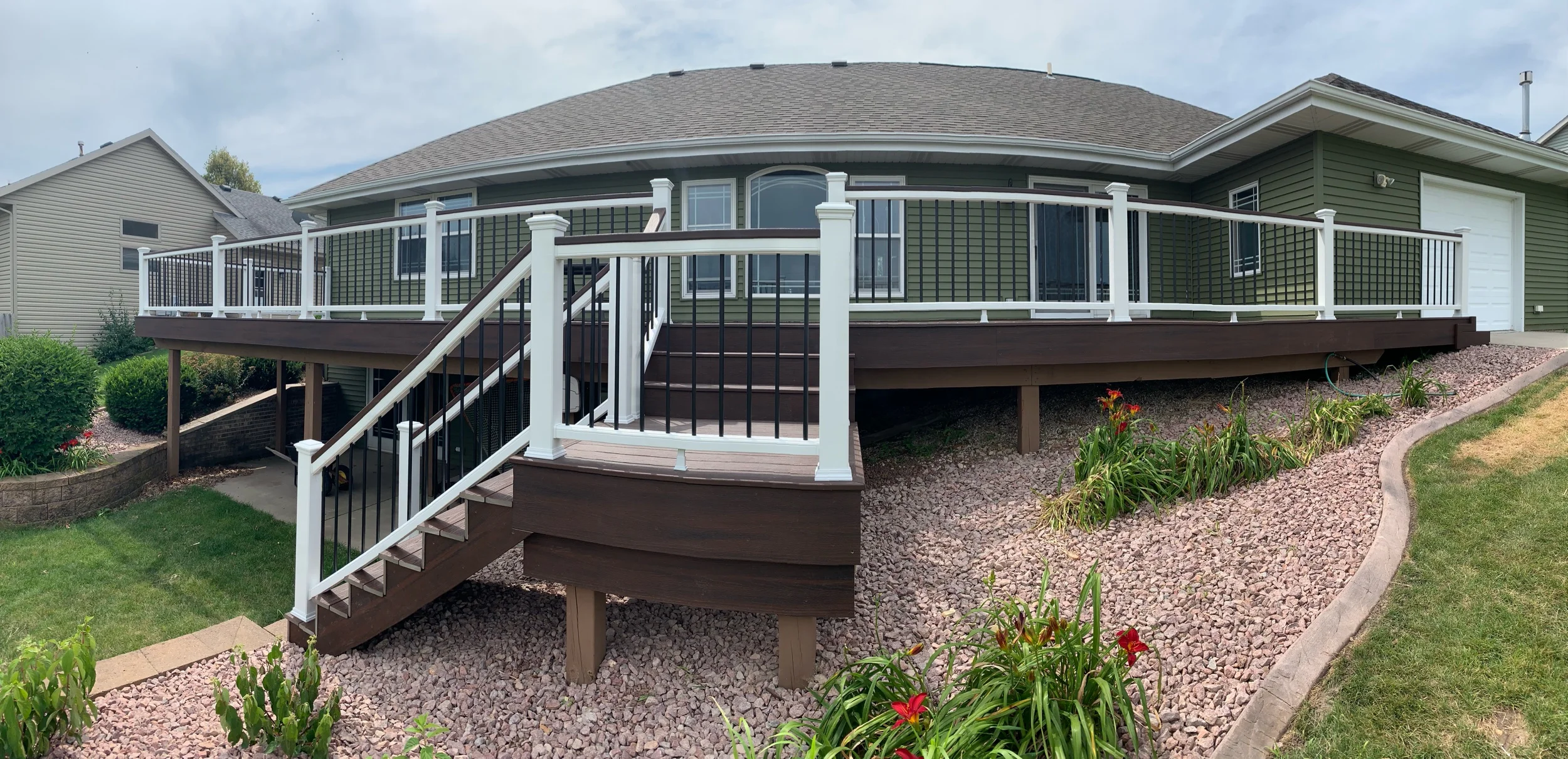 Trex Lava Rock deck boards with white top and bottom rails, Lava Rock drink rail on top of railings, black aluminum balusters and white post sleeves, post skirts, post caps. Double picture frame around perimeter of deck.