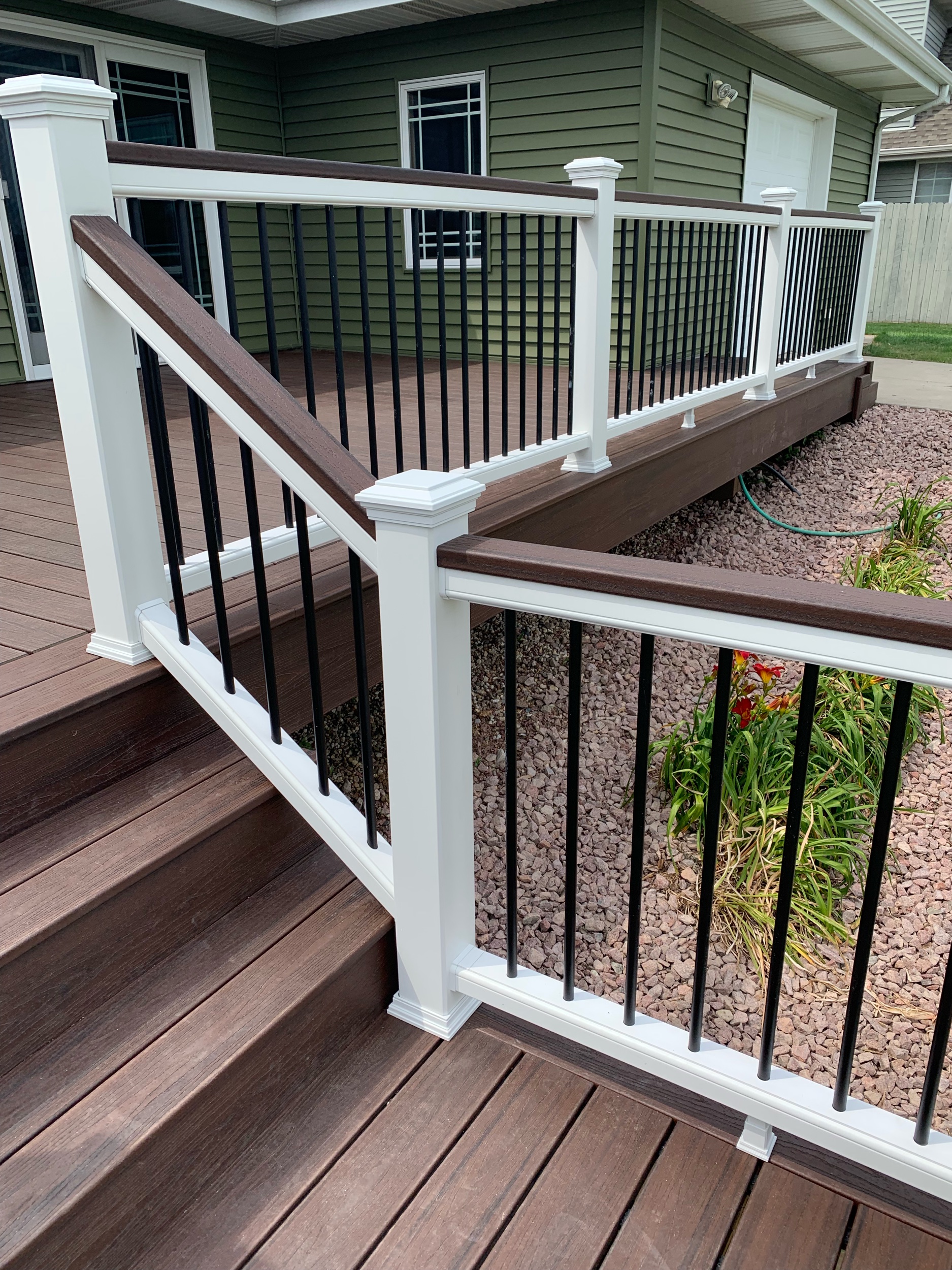 Trex Lava Rock deck boards with white top and bottom rails, Lava Rock drink rail on top of railings, black aluminum balusters and white post sleeves, post skirts, post caps. Double picture frame around perimeter of deck.