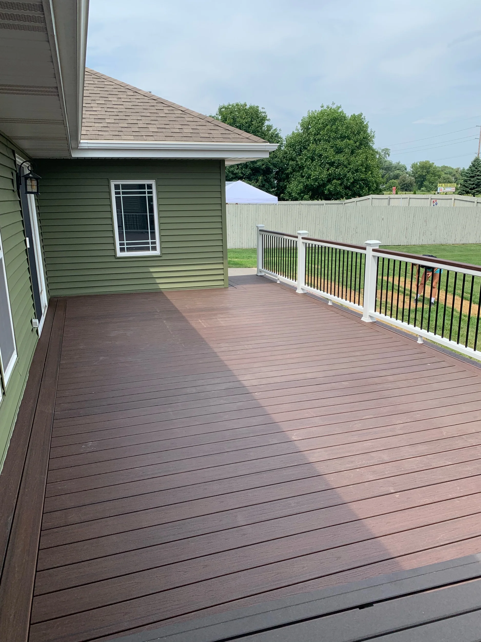 Trex Lava Rock deck boards with white top and bottom rails, Lava Rock drink rail on top of railings, black aluminum balusters and white post sleeves, post skirts, post caps. Double picture frame around perimeter of deck. 
