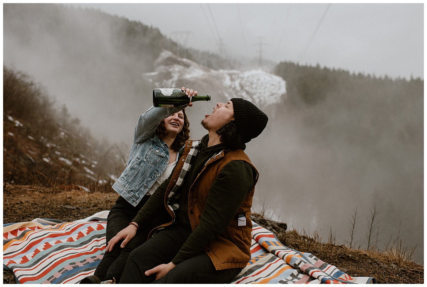 engaged couple popping champagne on a picnic blanket during their mt hood engagement session 