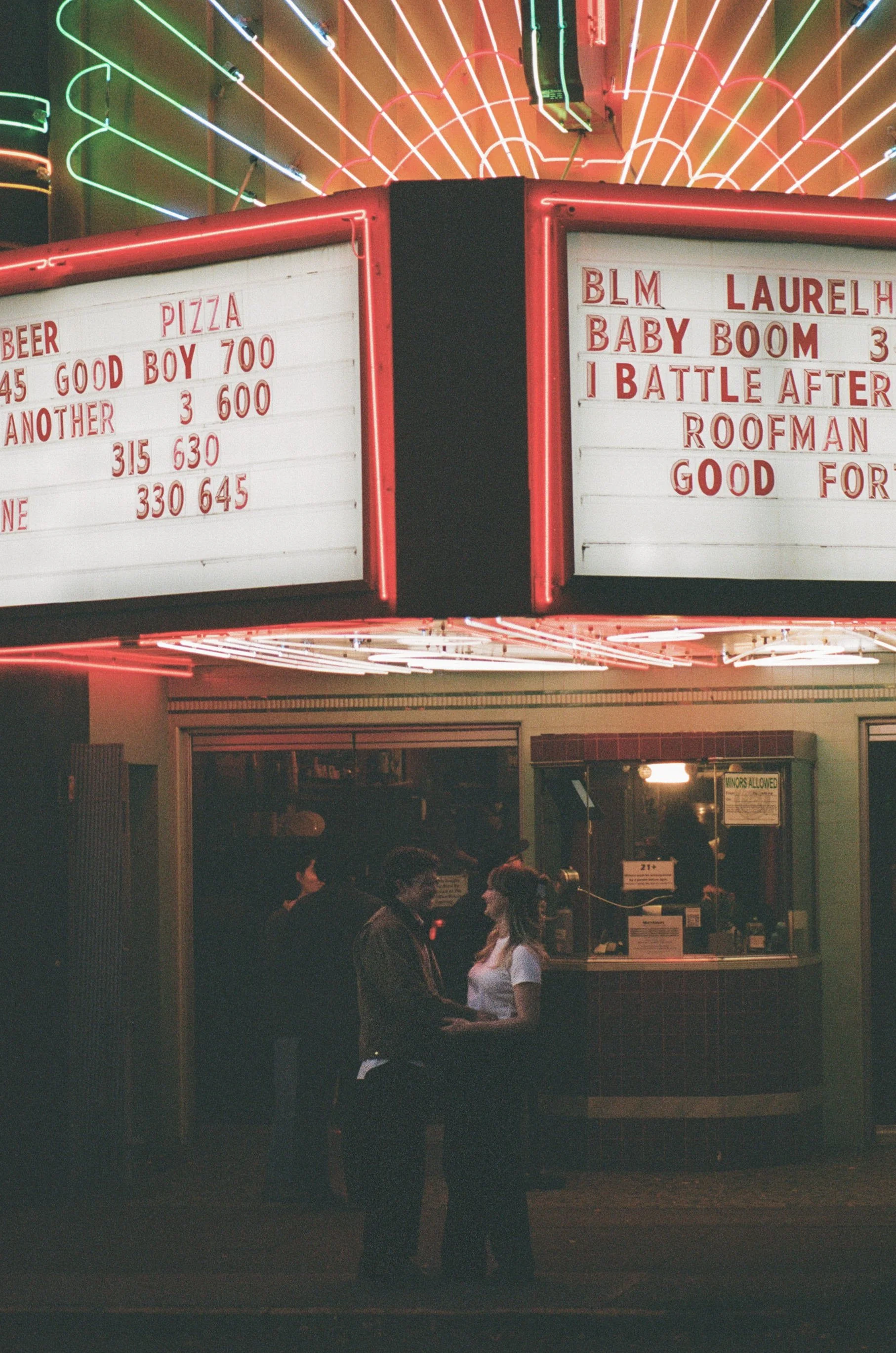  couple outside Laurelhurst Theater Portland under neon marquee lights at night, cinematic engagement photo shot on 35mm film 