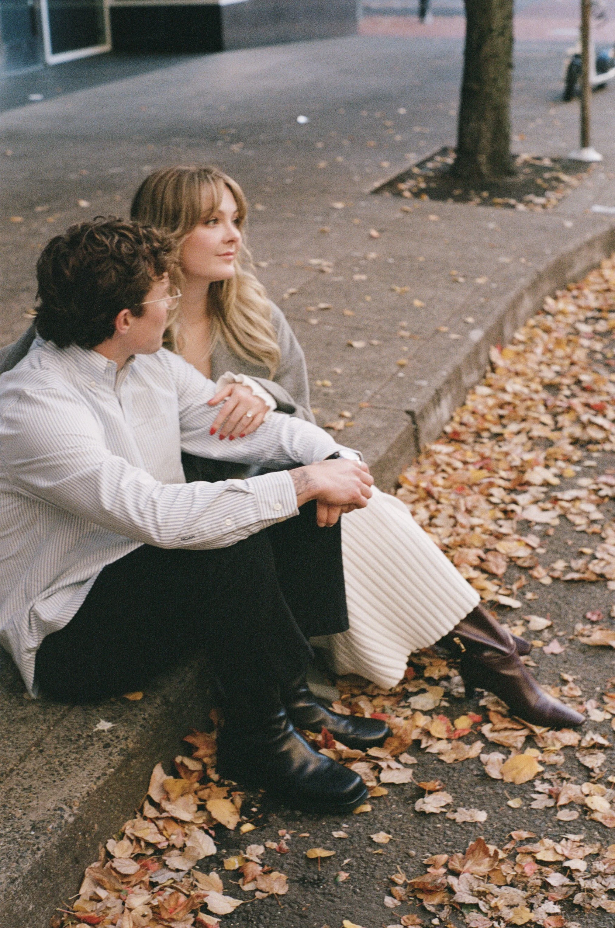 couple walking through downtown Portland in autumn with golden leaves and modern architecture, candid engagement photography 