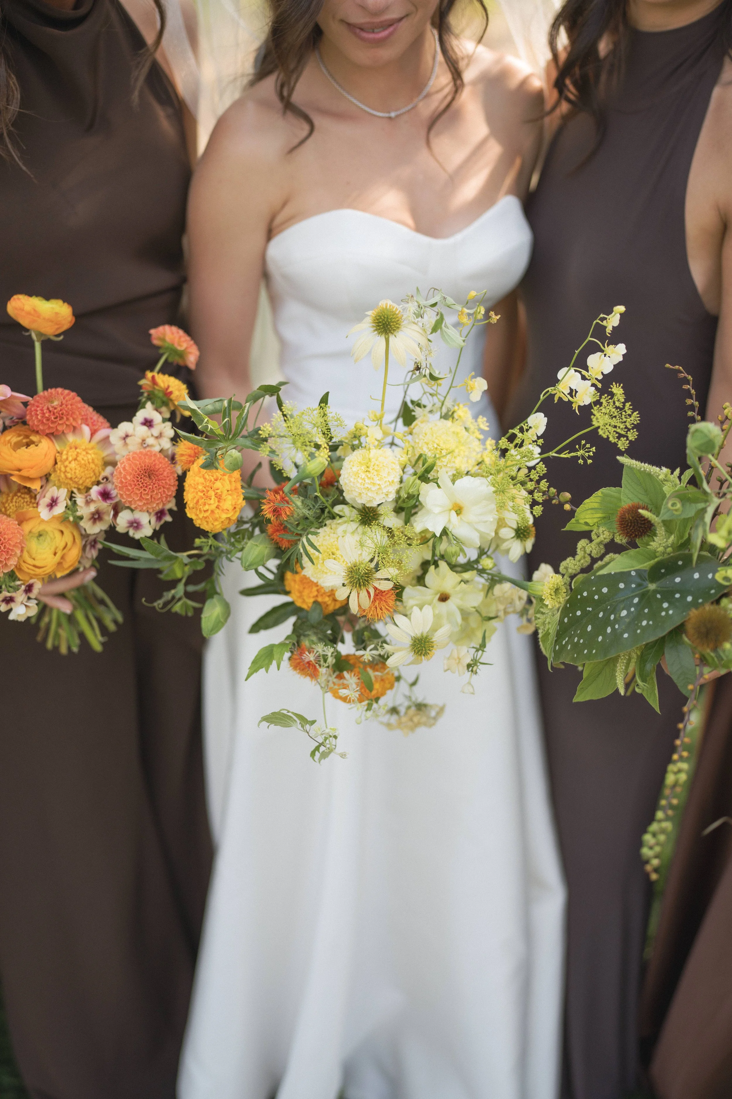  Bridesmaids in chocolate brown dresses holding colorful bouquets with orange and green tones 