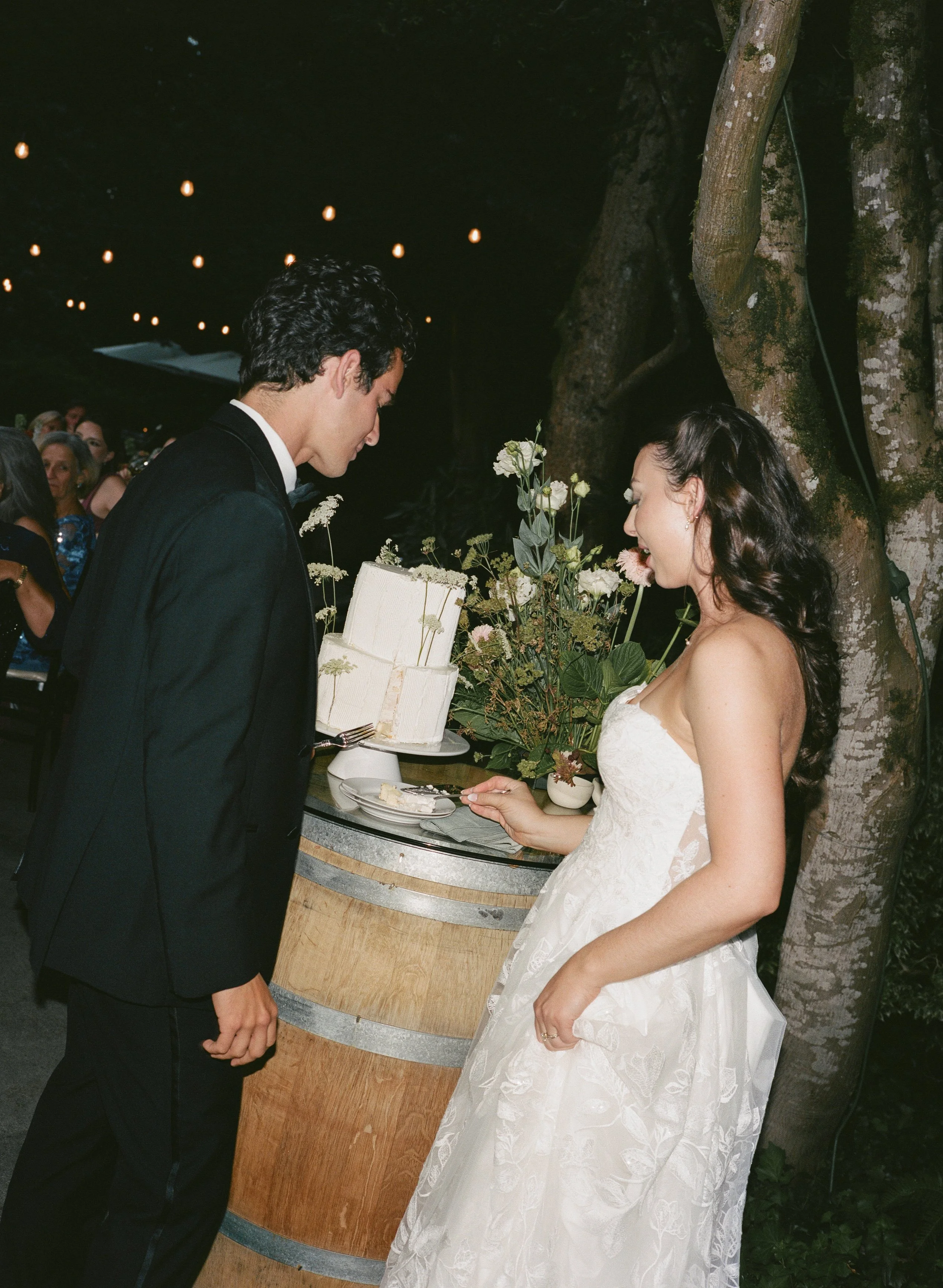  Film wedding photography at JM Cellars capturing a romantic outdoor celebration surrounded by trees and ivy. Bride and groom cake cutting 