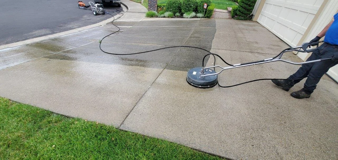 A person using a power concrete grinder to smooth a concrete driveway and sidewalk outside a house.