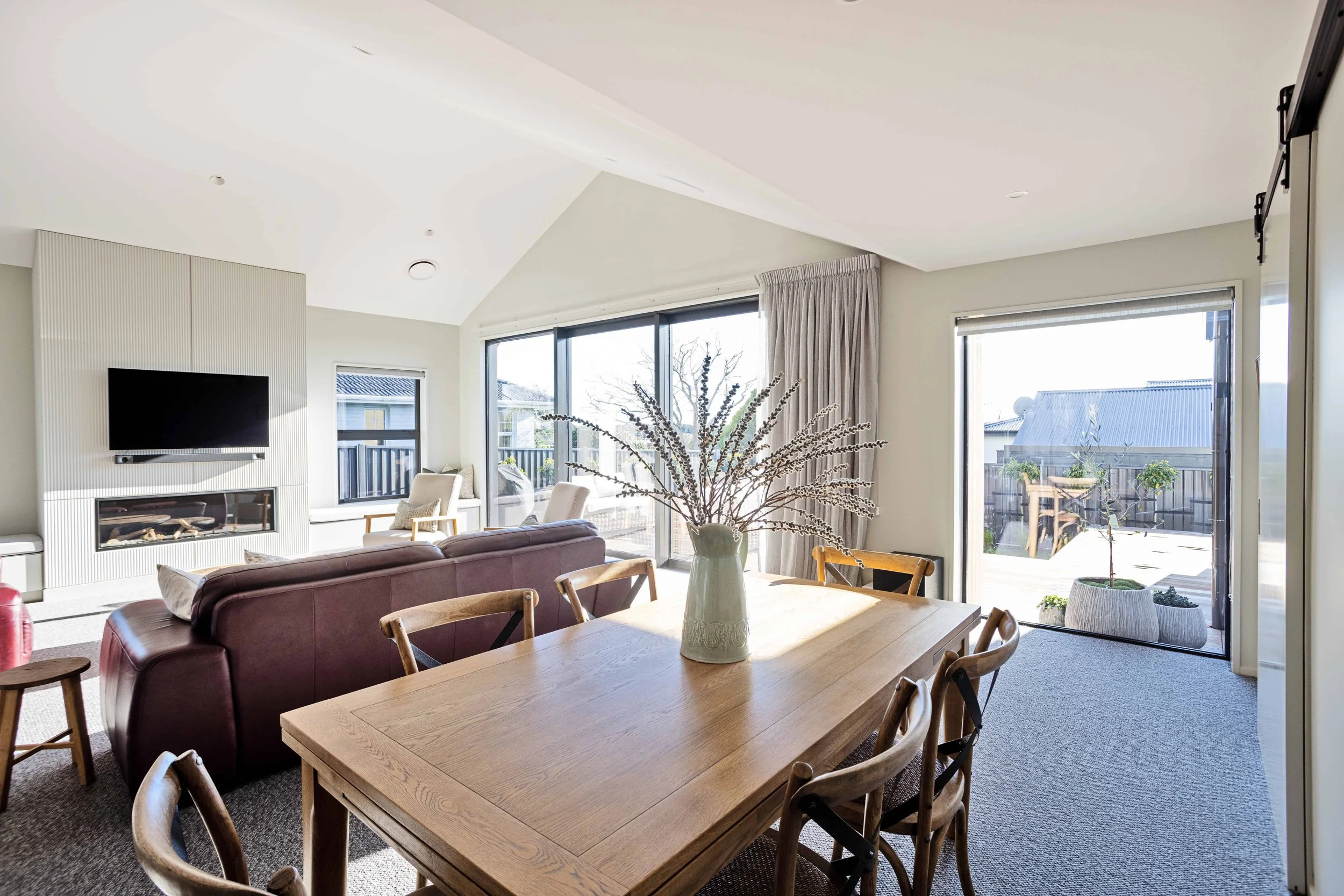 Living room with a dining table, chairs, a purple sofa, and large windows overlooking a backyard.