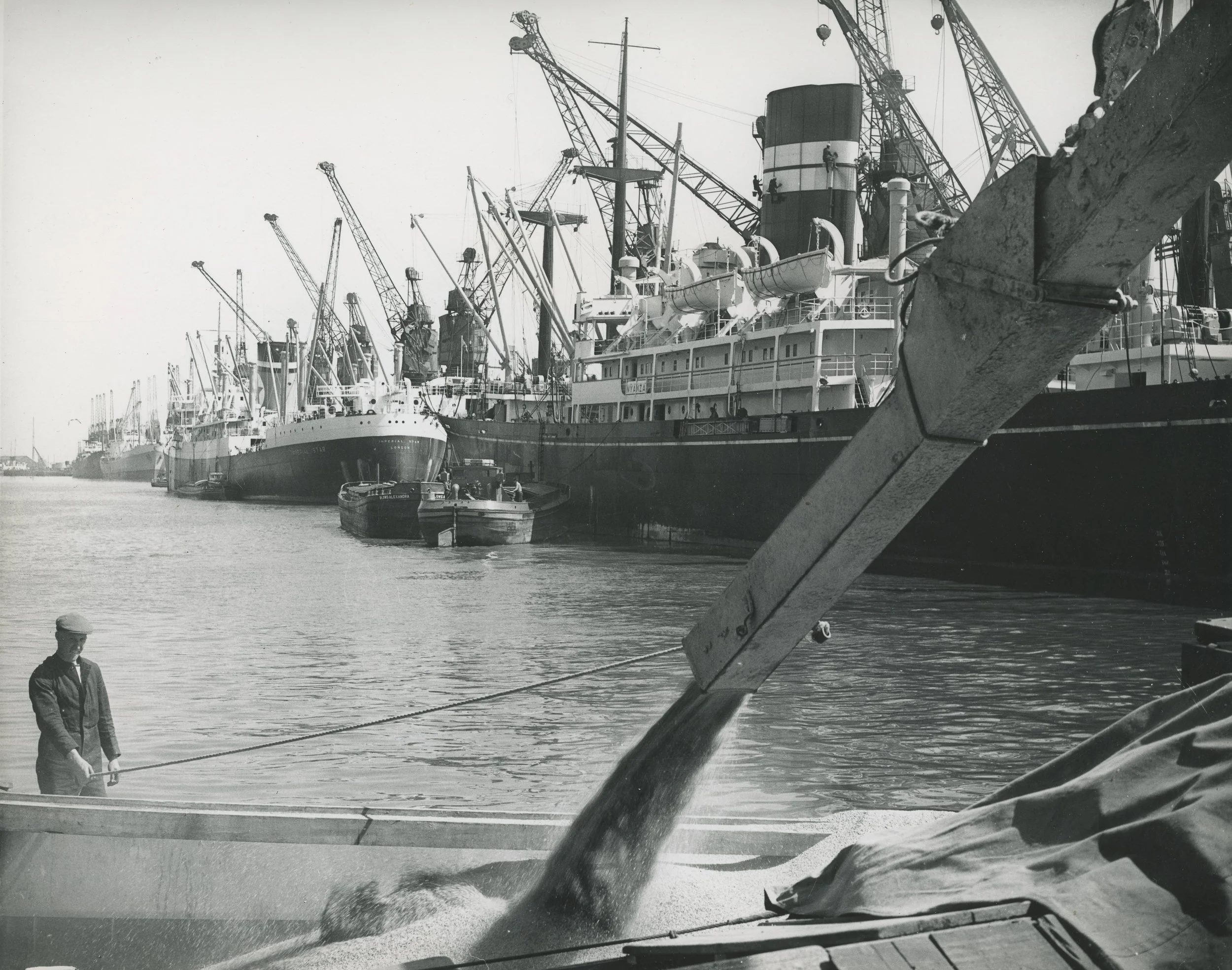 A worker overseeing the discharge of grain from silo to craft. King George Dock, Hull. June, 1960. Photographer - Donald I. Innes Commissioned by ABP.