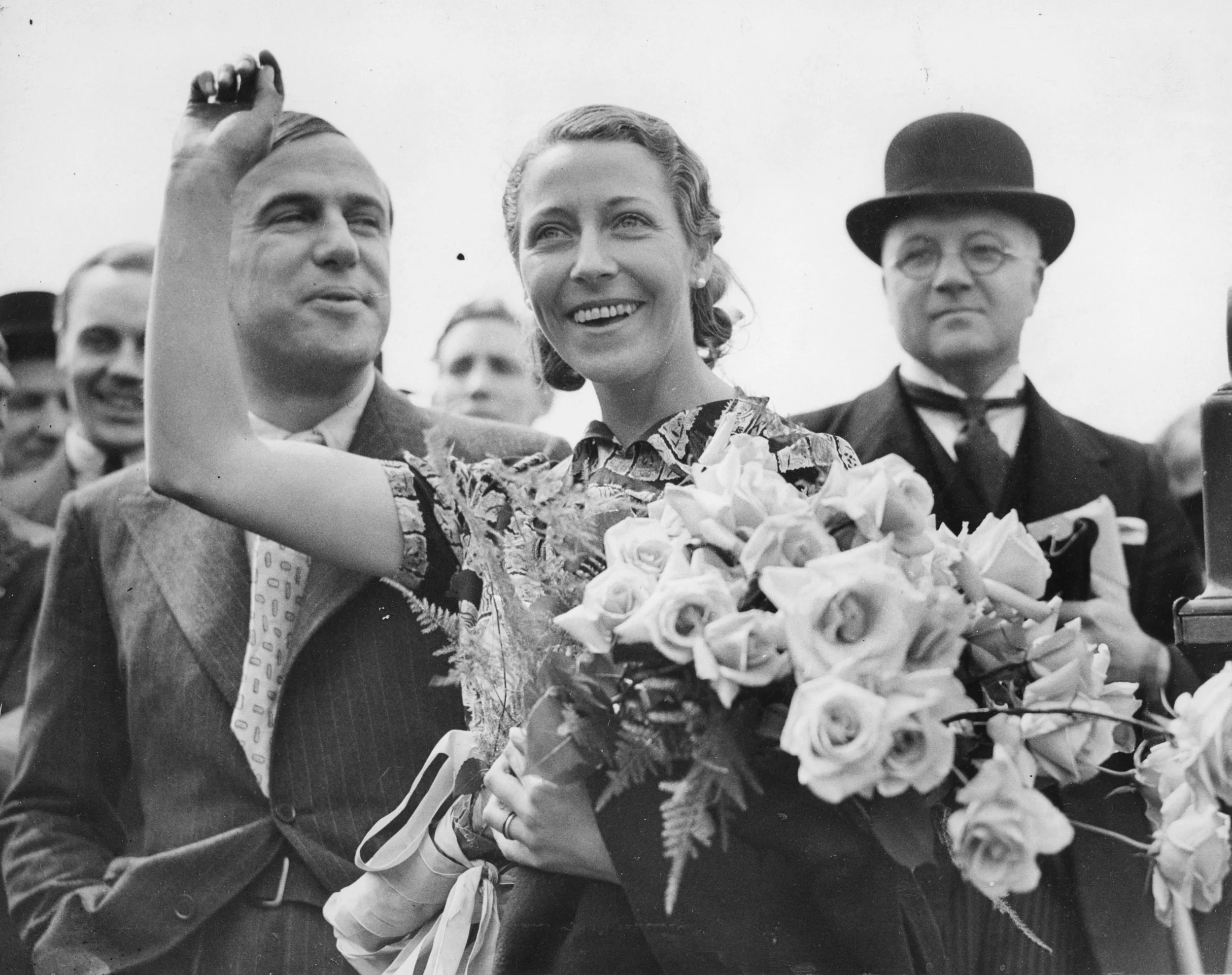 Amy Johnson and Jim Mollison at Croydon, after her record-breaking flight from Capetown, 15-05-1936. Amy is wearing her 'airmail stamp' print blouse. "Amy Mollison smashes Cape to London Record by Day and a Half." Commissioned by Hull Daily Mail.