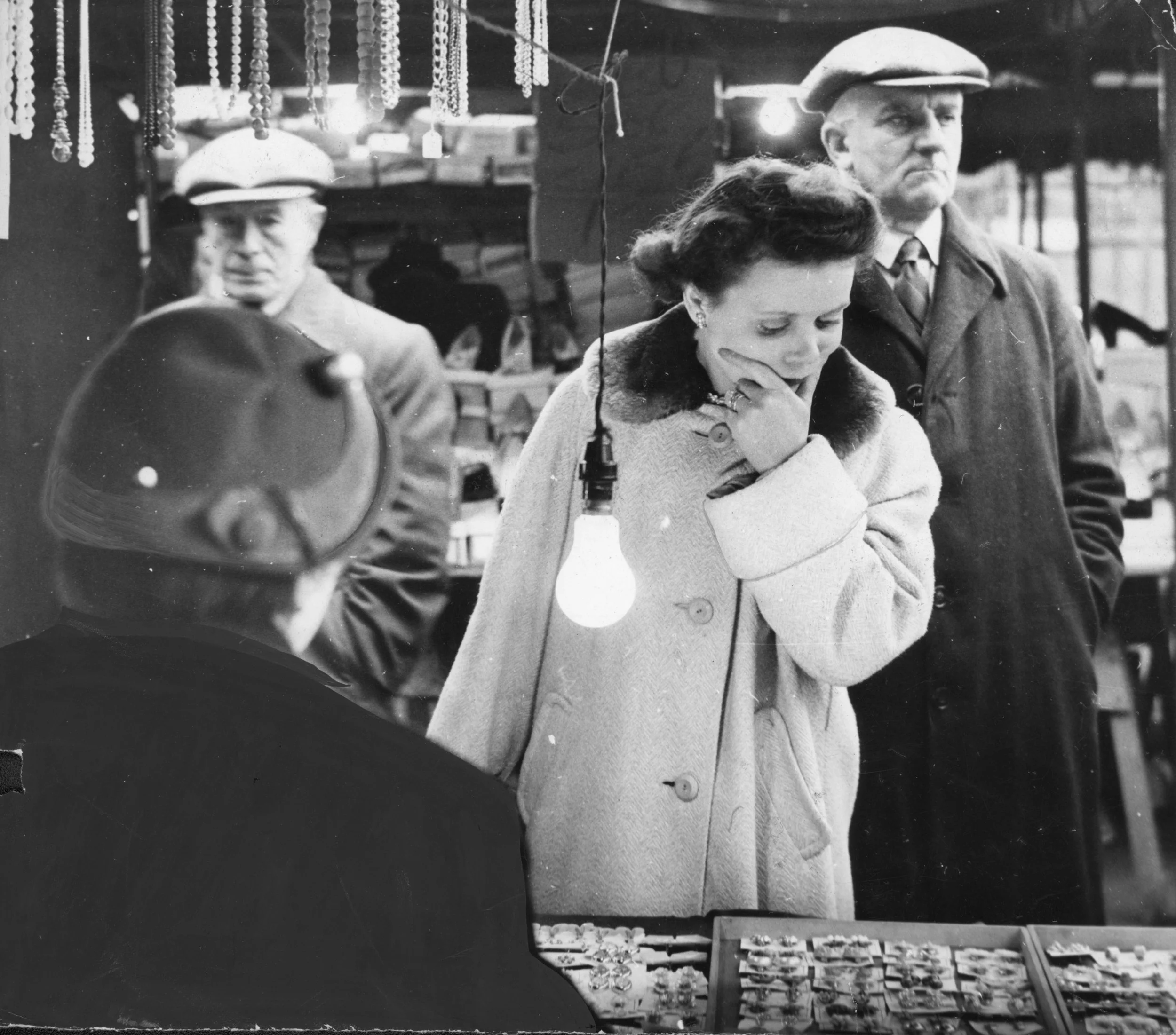 A woman in a coat with a fur collar, shopping for earrings at a stall in Hull Market, 16-02-1957. Commissioned by Hull Daily Mail.