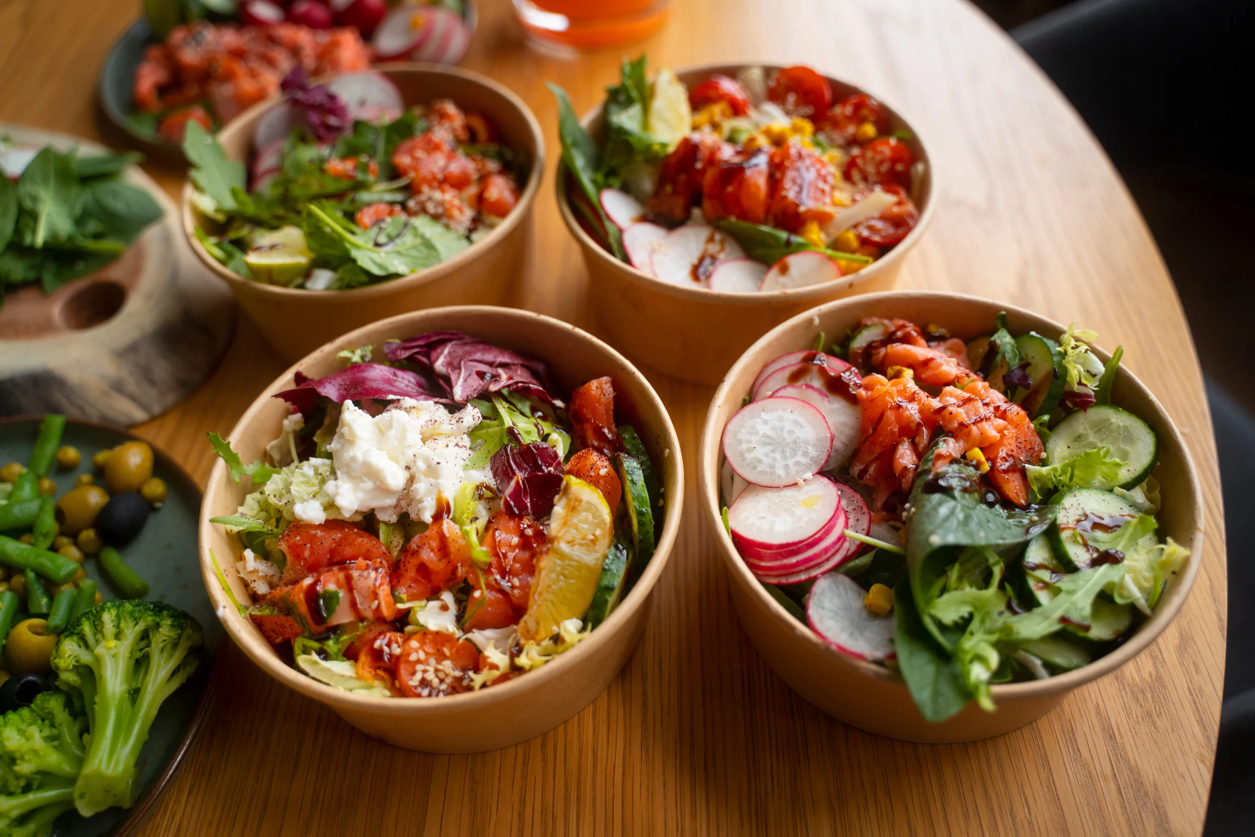 Multiple bowls of fresh salad with various vegetables and toppings on a wooden table.